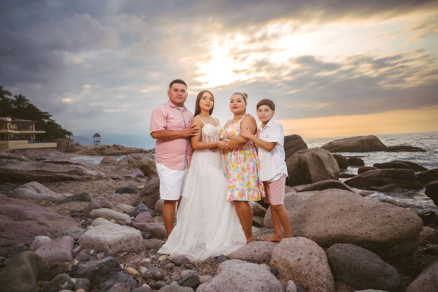 Sunset family portrait session on rocky coastal beach with dramatic sky.