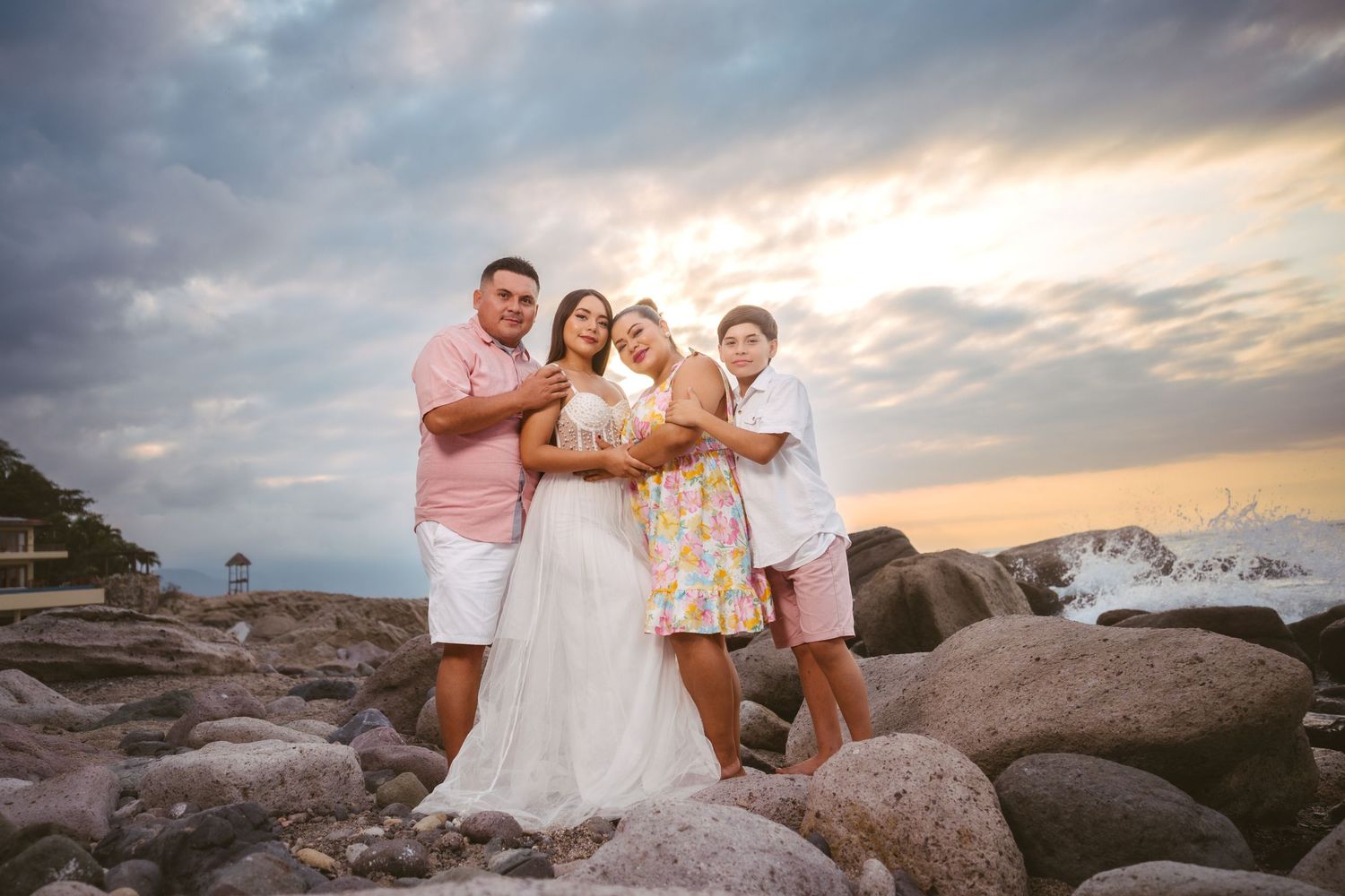 Family group poses on rocky beach during golden hour with ocean backdrop.