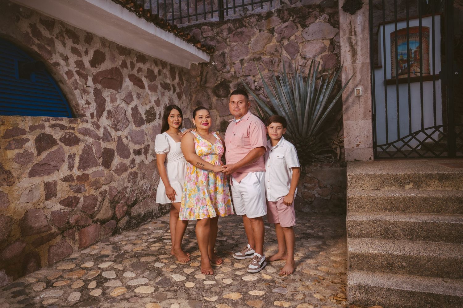 Children in white outfits pose playfully against a rustic stone wall during a family photo session.