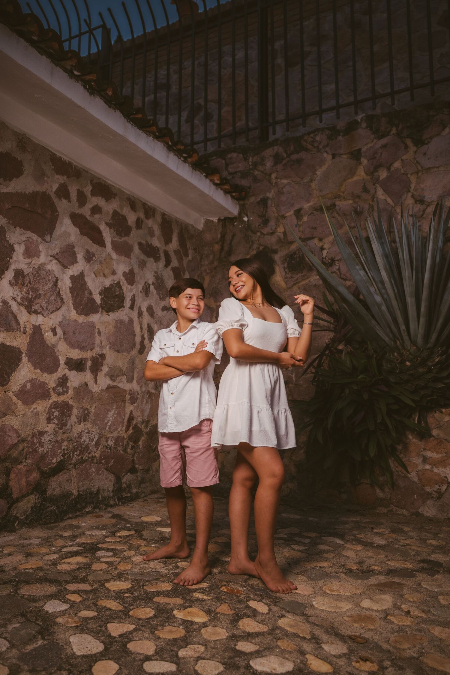 Playful interaction between young siblings against a stone wall with decorative plants.