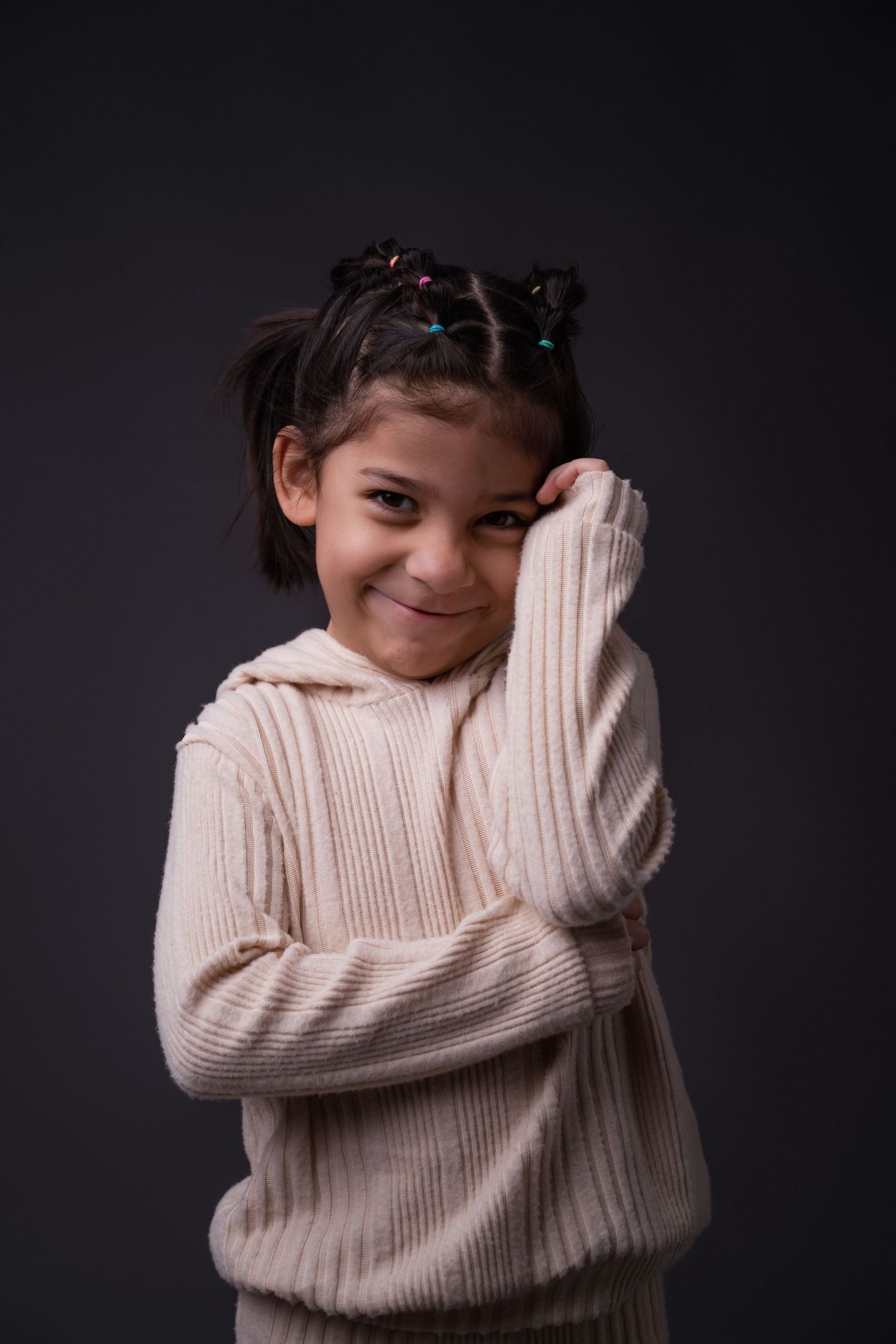 Person in a cream ribbed sweater hugging themselves while smiling against dark background.