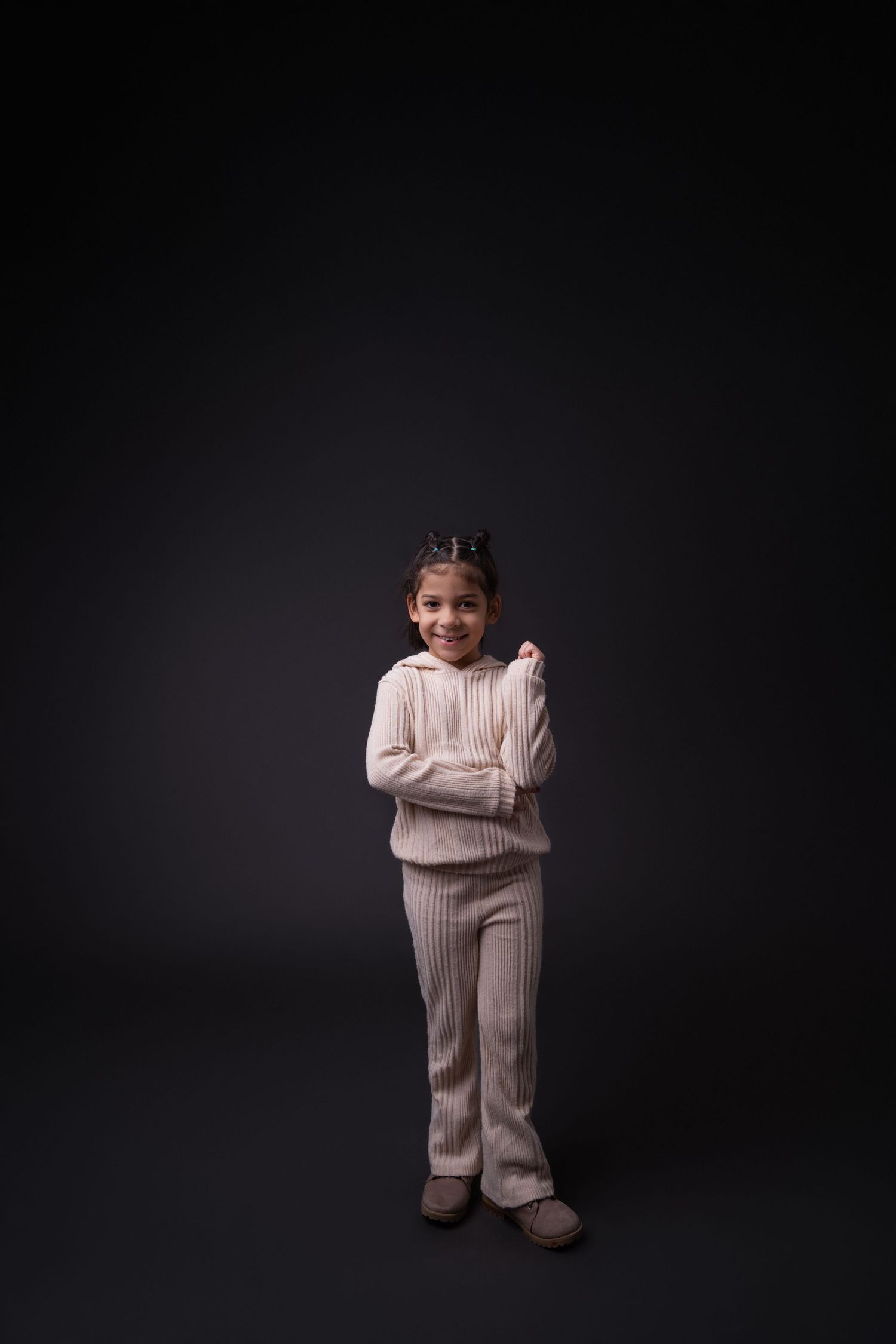 Person wearing cozy beige knit outfit poses playfully against dark studio backdrop.