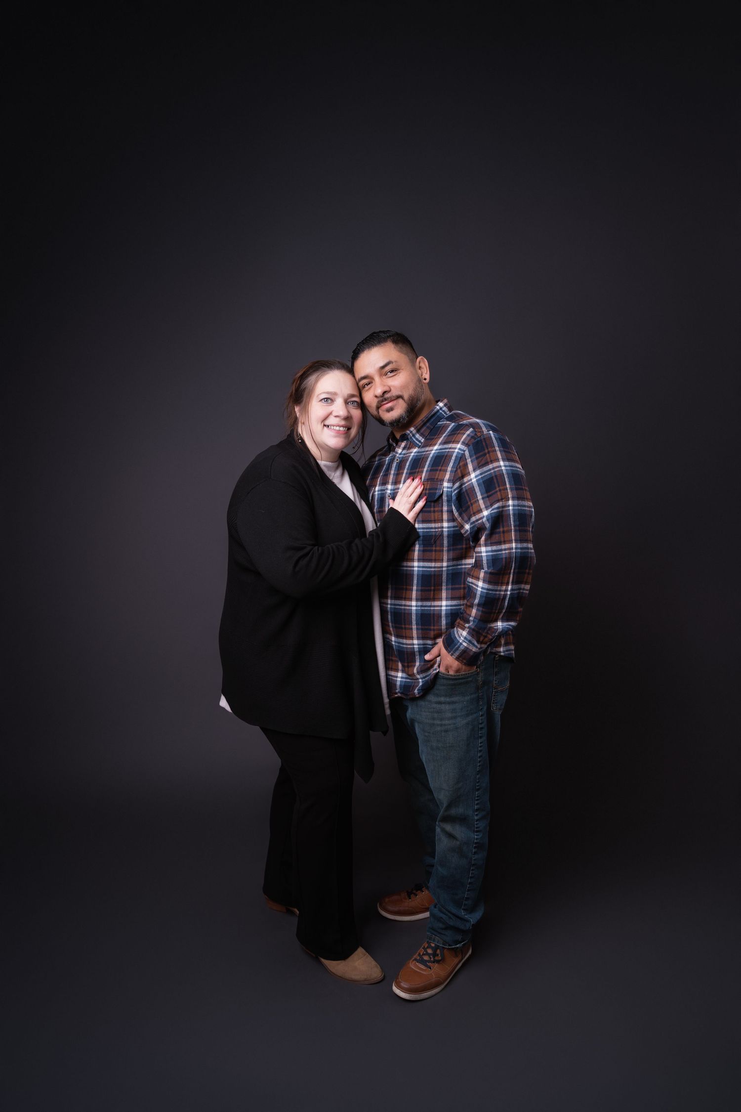 Two people share an affectionate moment against dark studio background.