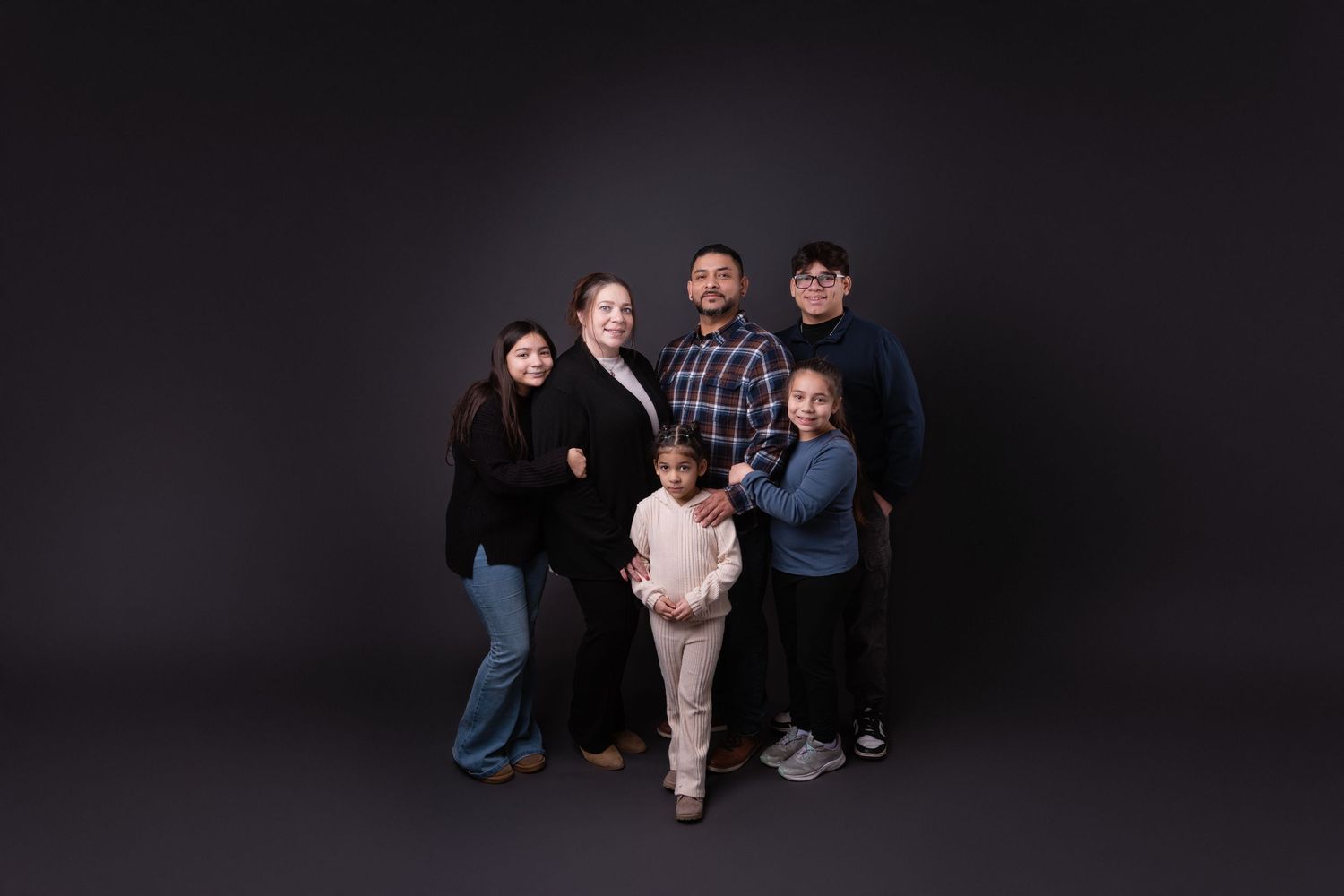 Family portrait with multiple members arranged in casual poses against dark backdrop.