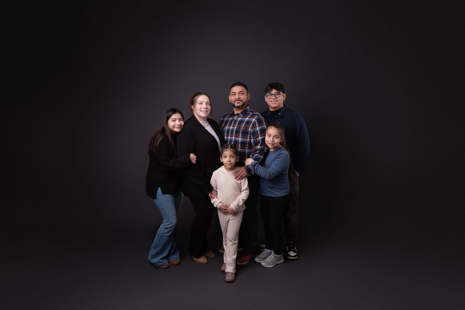 Studio family photo with group members arranged in casual formation against dark background.