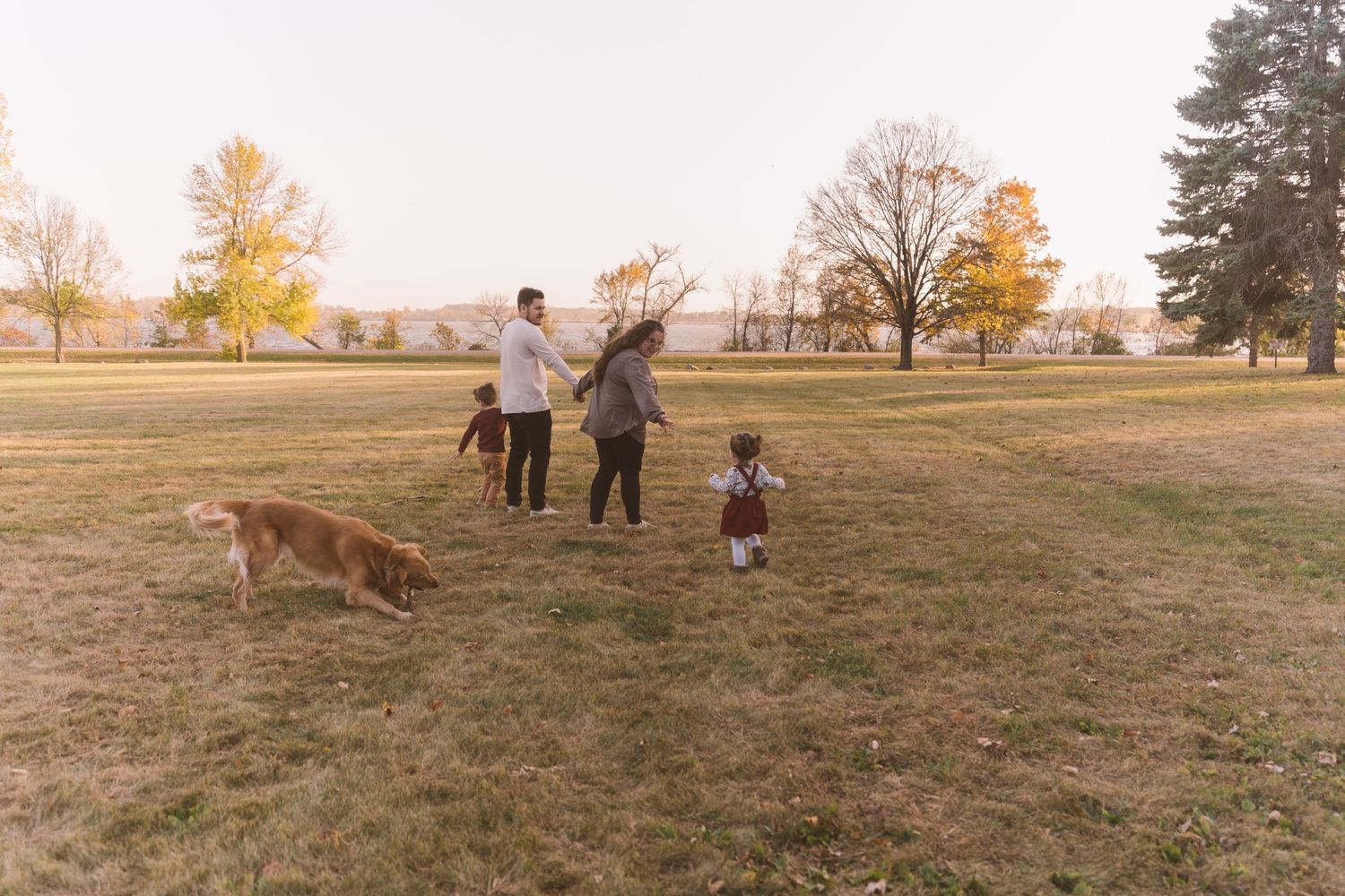 Family walking with dog in autumn field during golden hour sunset.