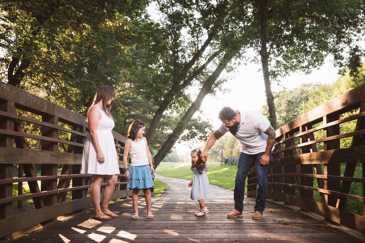 Groups walking along a scenic wooden bridge pathway under green tree canopy.