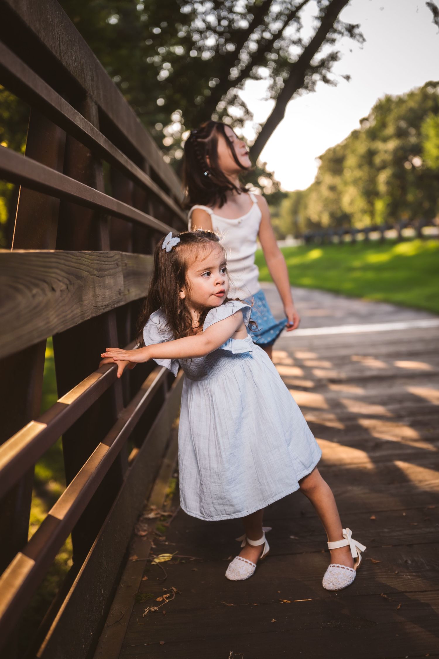Small child playfully looks through wooden bridge railings during golden hour.