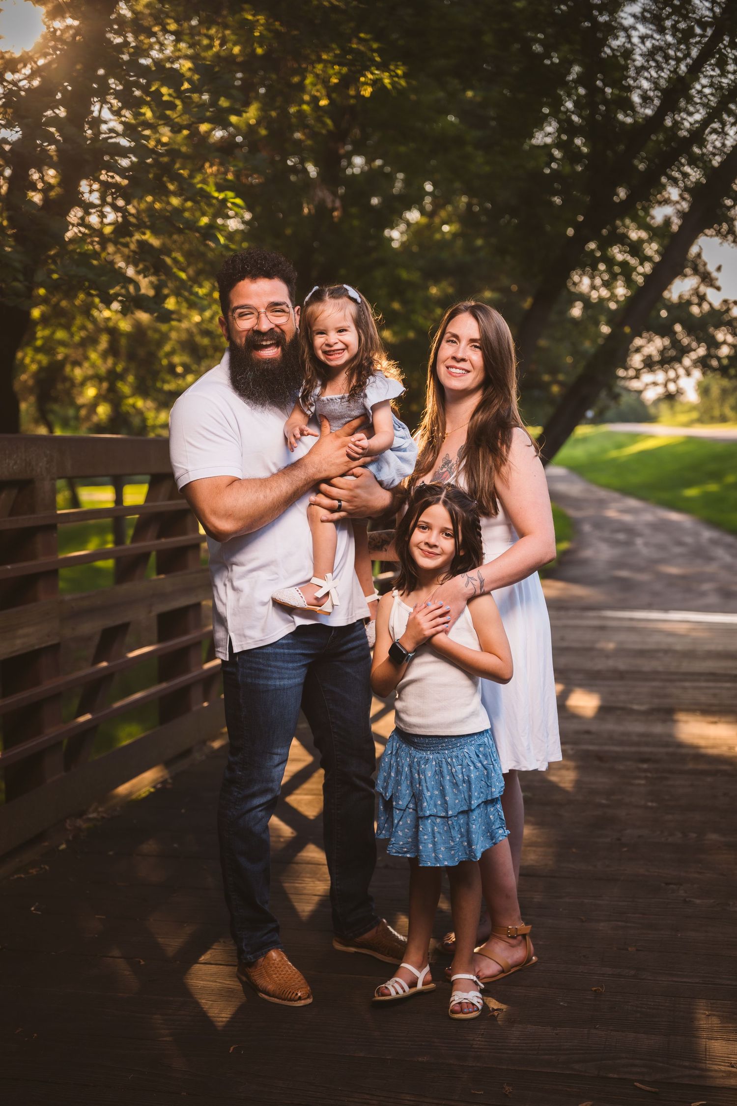 A joyful family shares laughter and hugs on a wooden bridge during golden hour.
