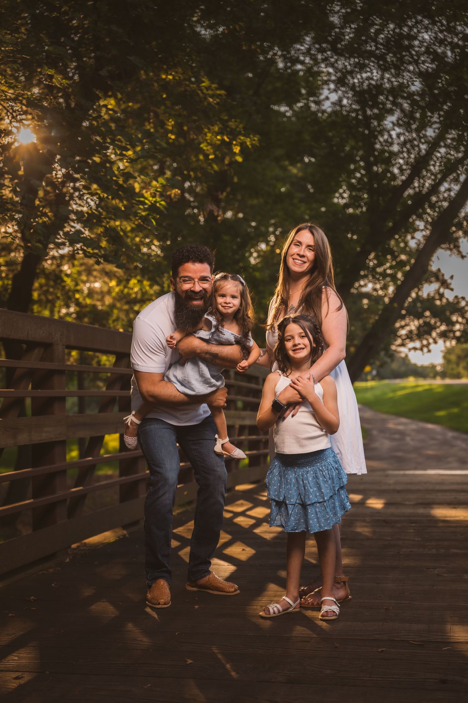 Playful family poses on wooden bridge during golden hour photography session.