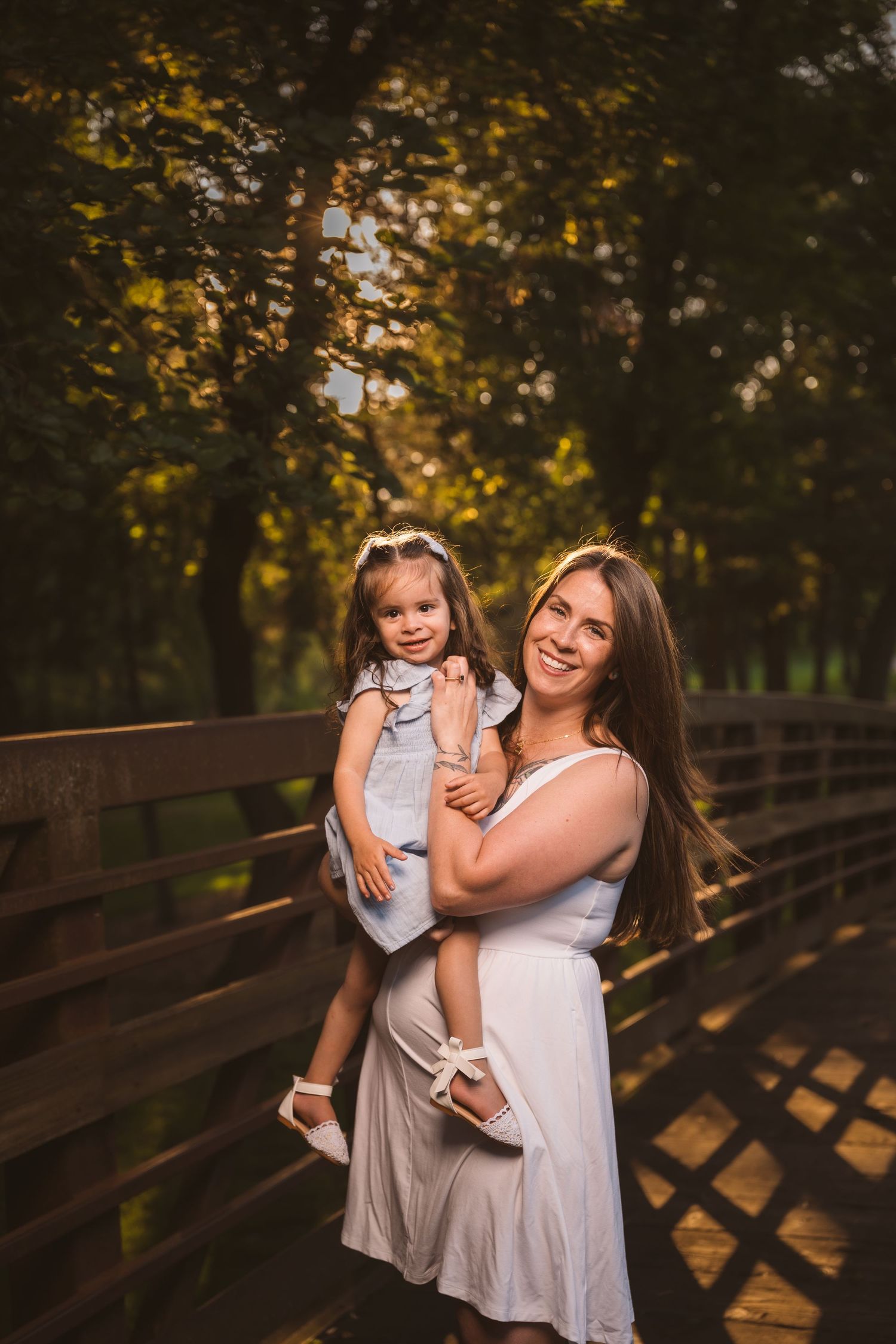 Family members share loving embrace on wooden bridge during sunset photoshoot.