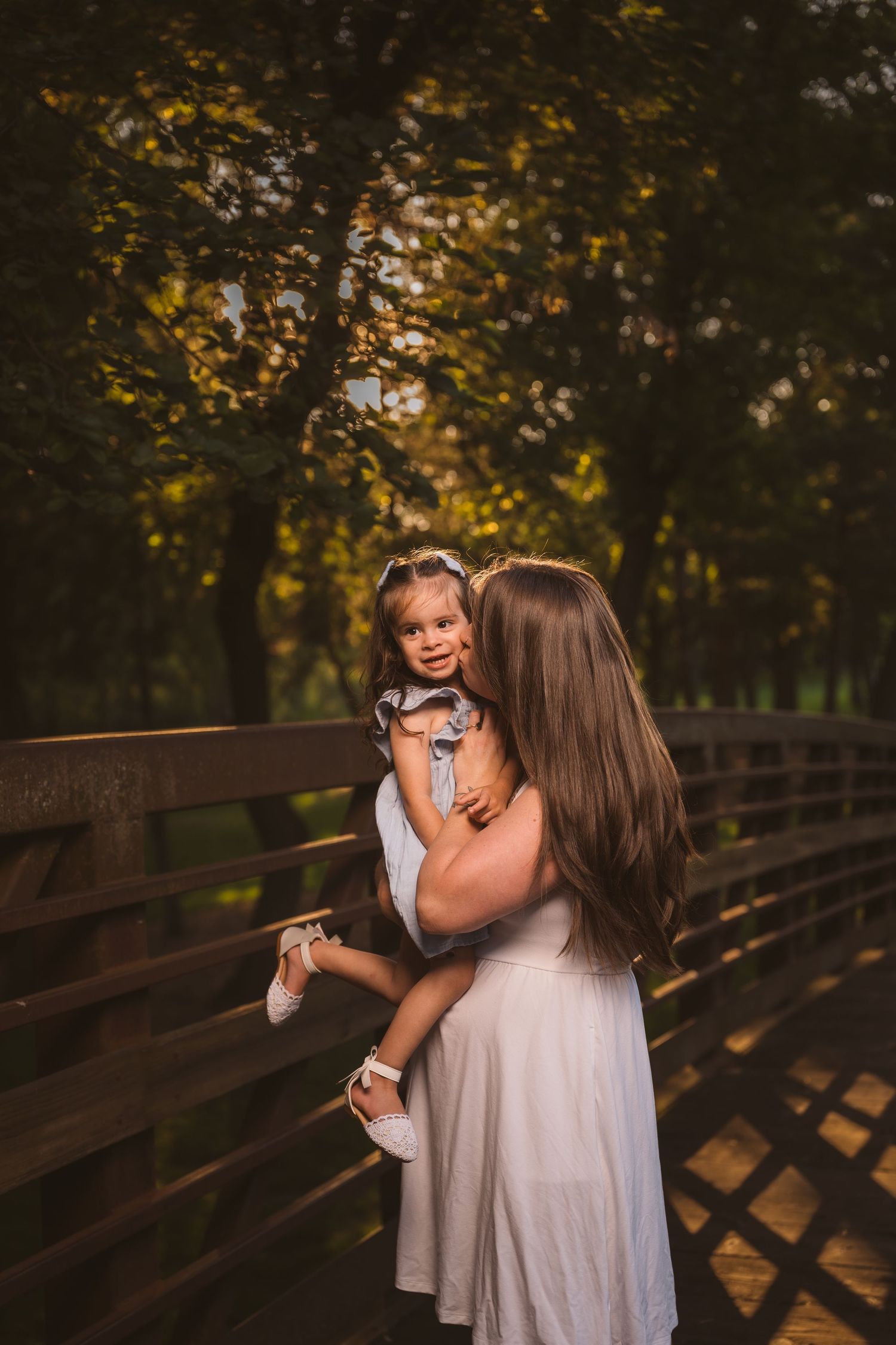 Tender moment between family members captured on wooden bridge at sunset.