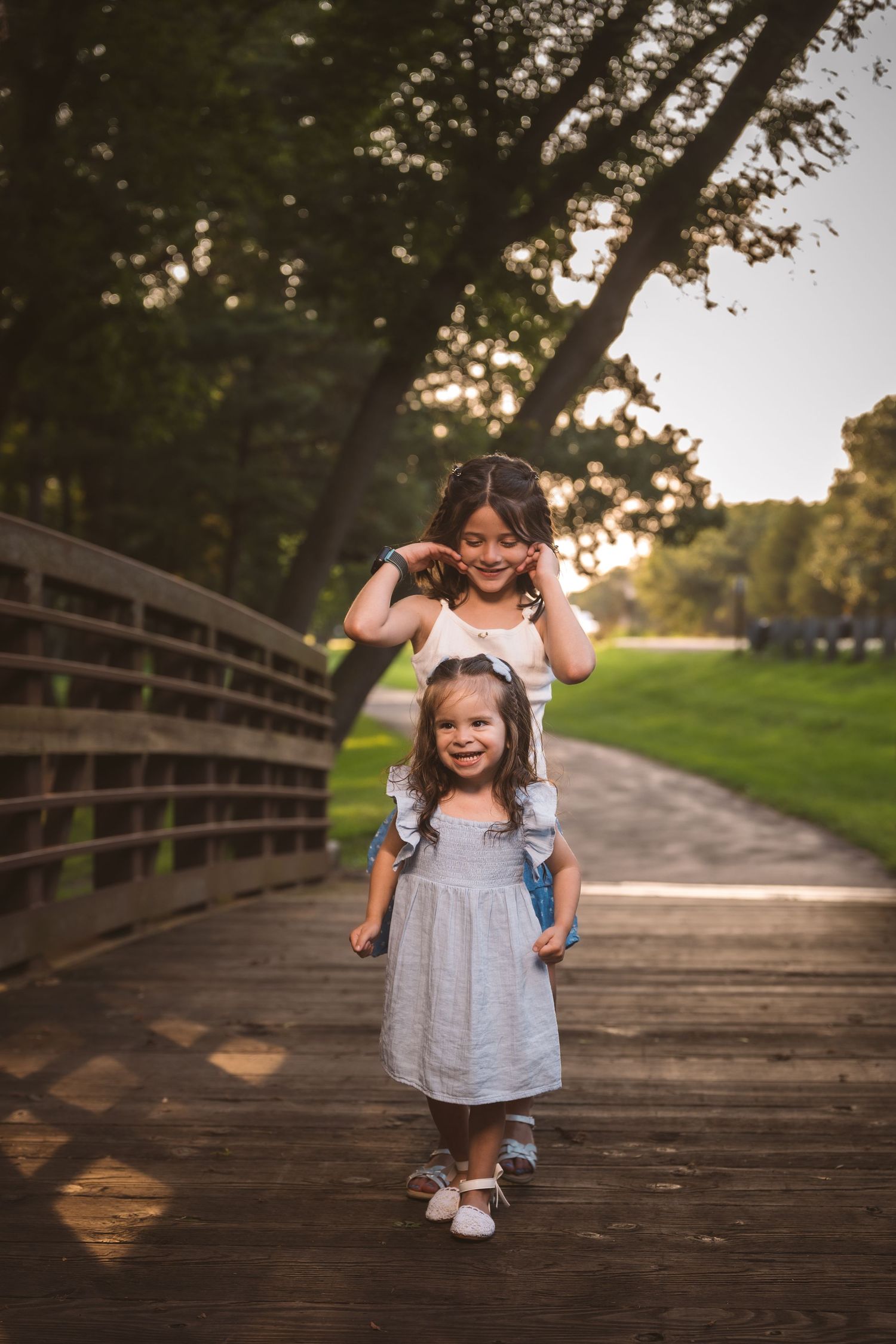 Children in summer outfits playing and laughing on a wooden boardwalk during golden hour.