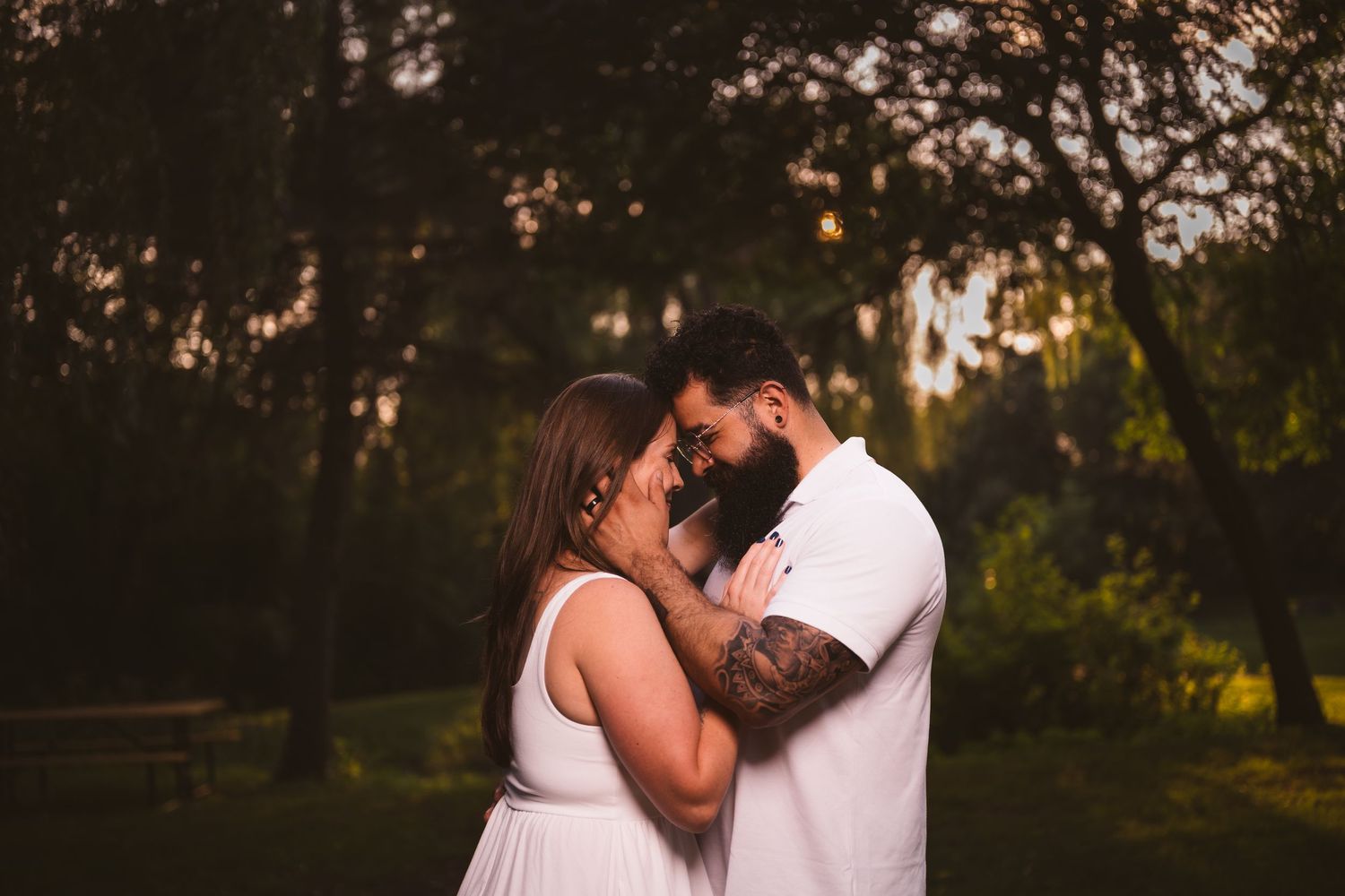 A romantic couple embracing in a park setting during sunset.