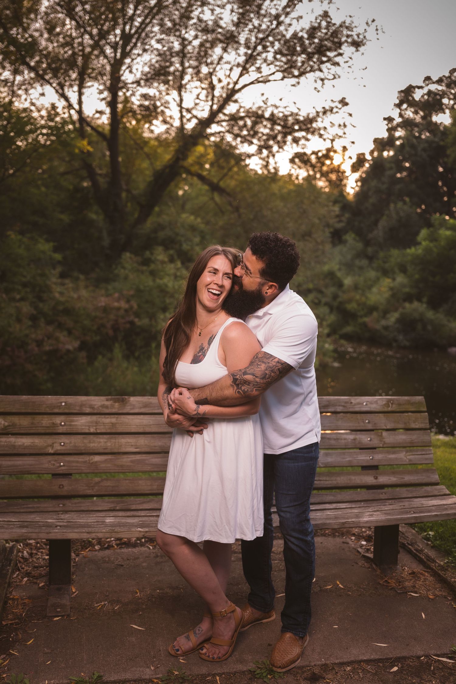 A couple sharing joyful moments on a wooden park bench during sunset.