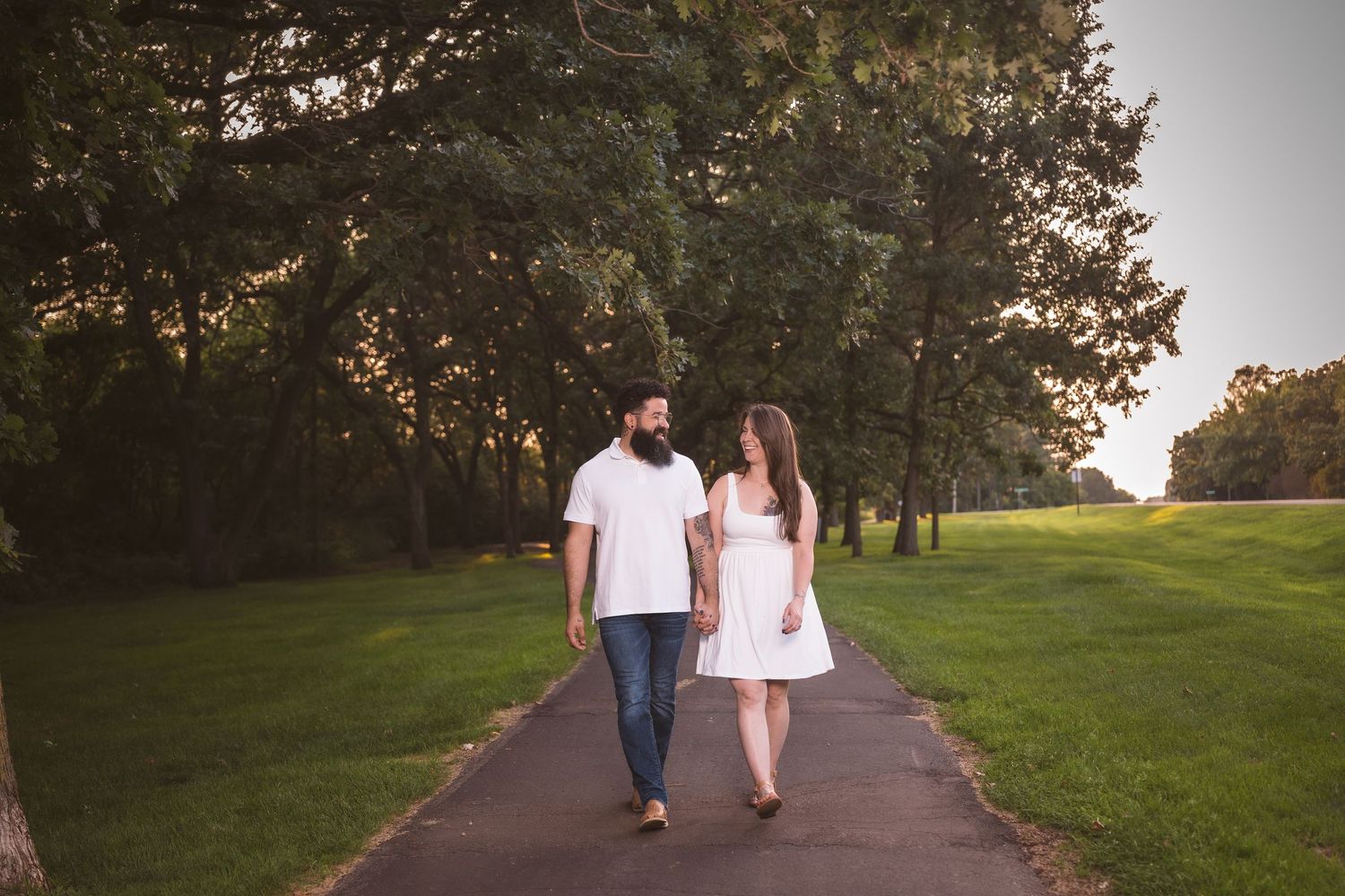 A couple walking together on a path through a green park at sunset.