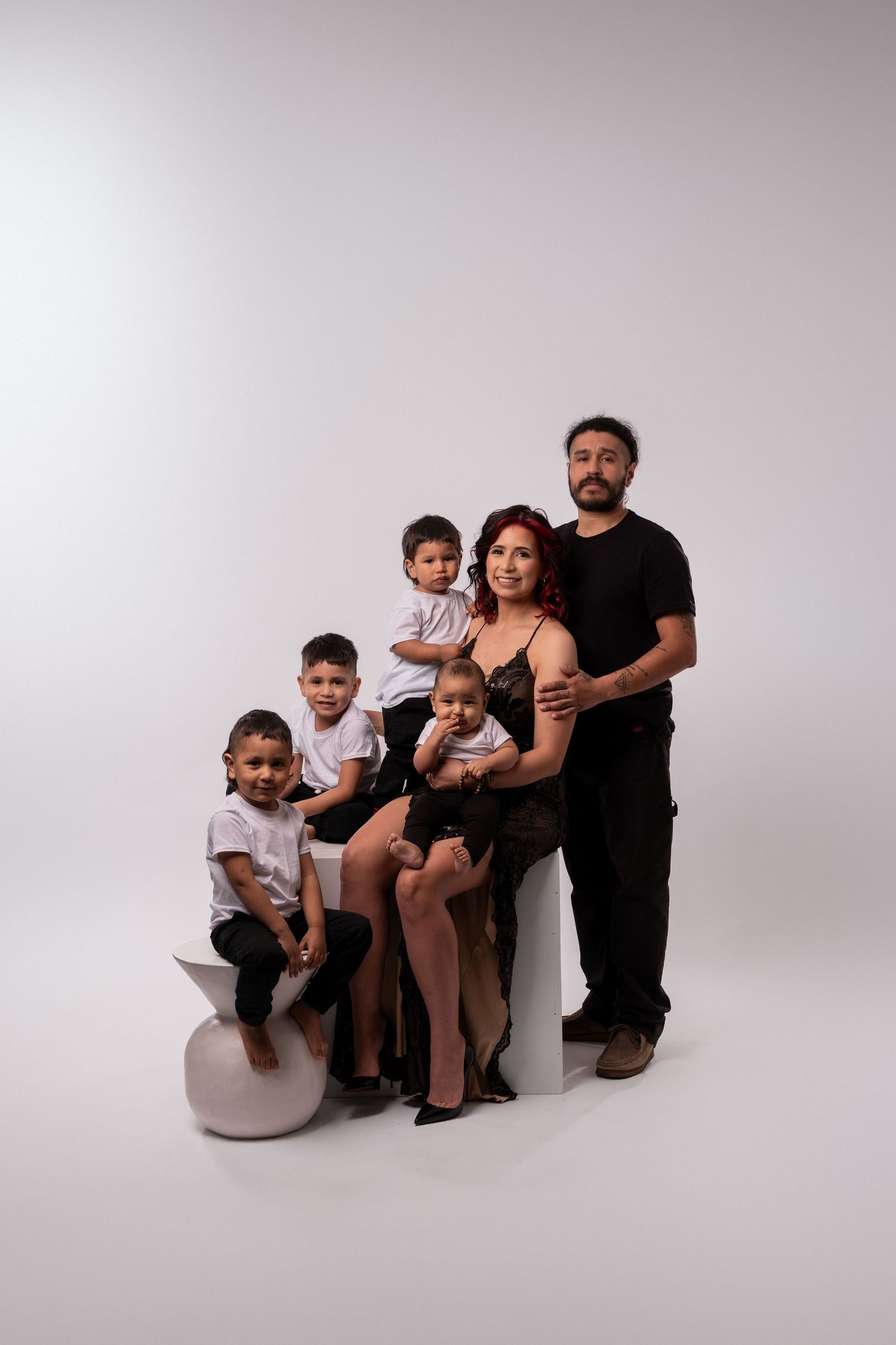 Family group sitting together on white platform in studio setting.