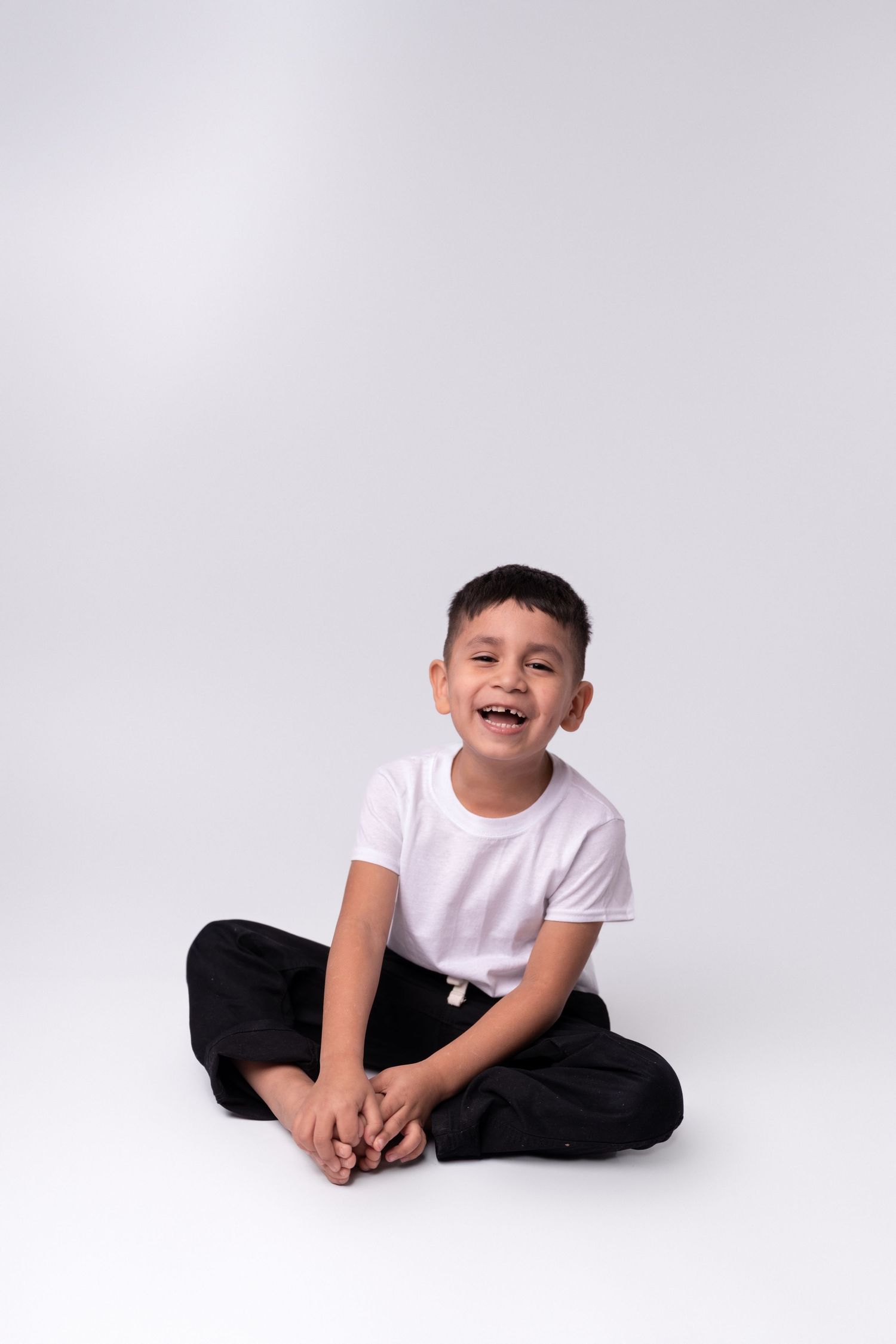 Child in white shirt and black pants showing joyful expressions on white background.