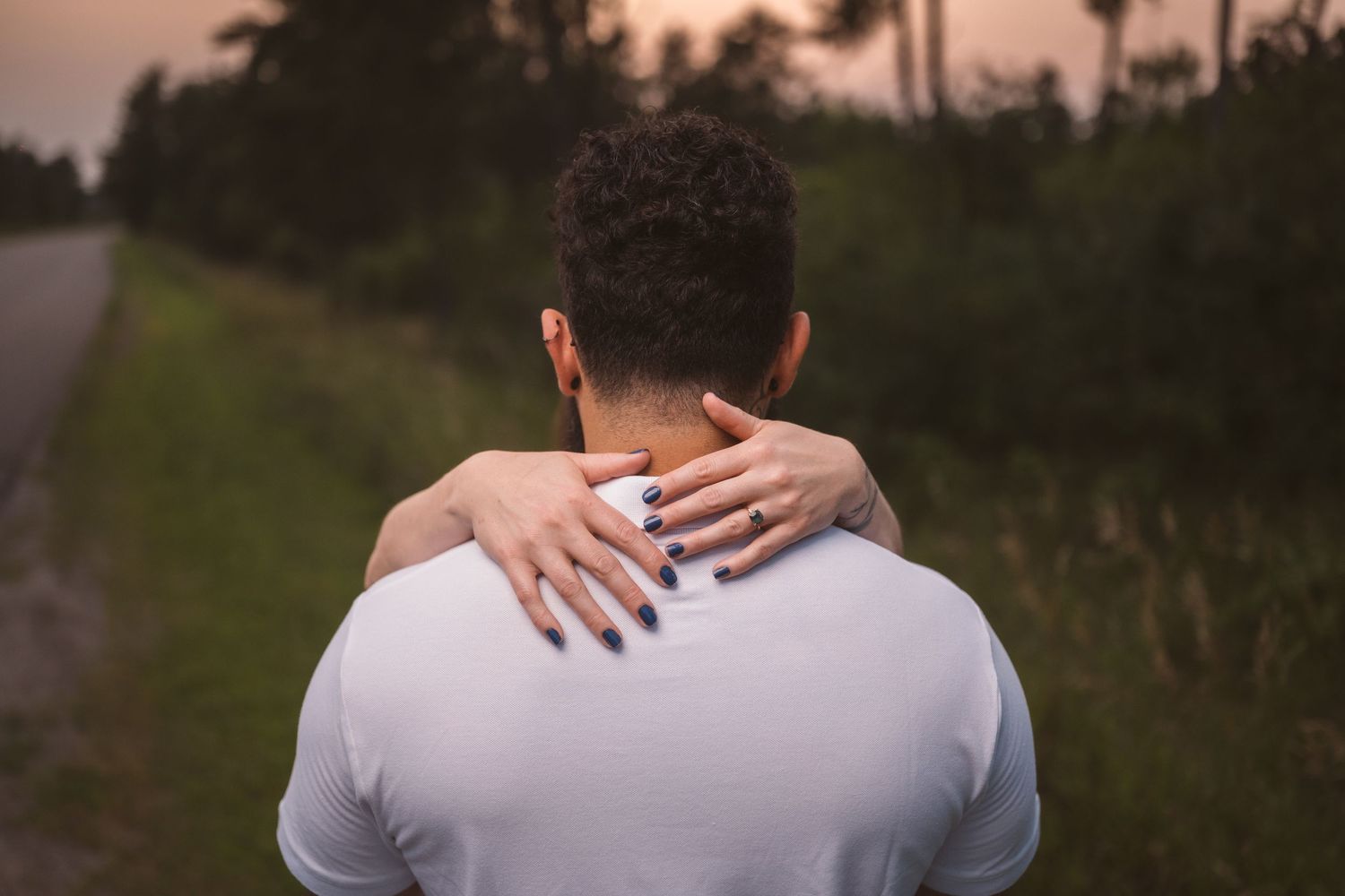 A close-up detail of hands embracing against a sunset backdrop in nature.