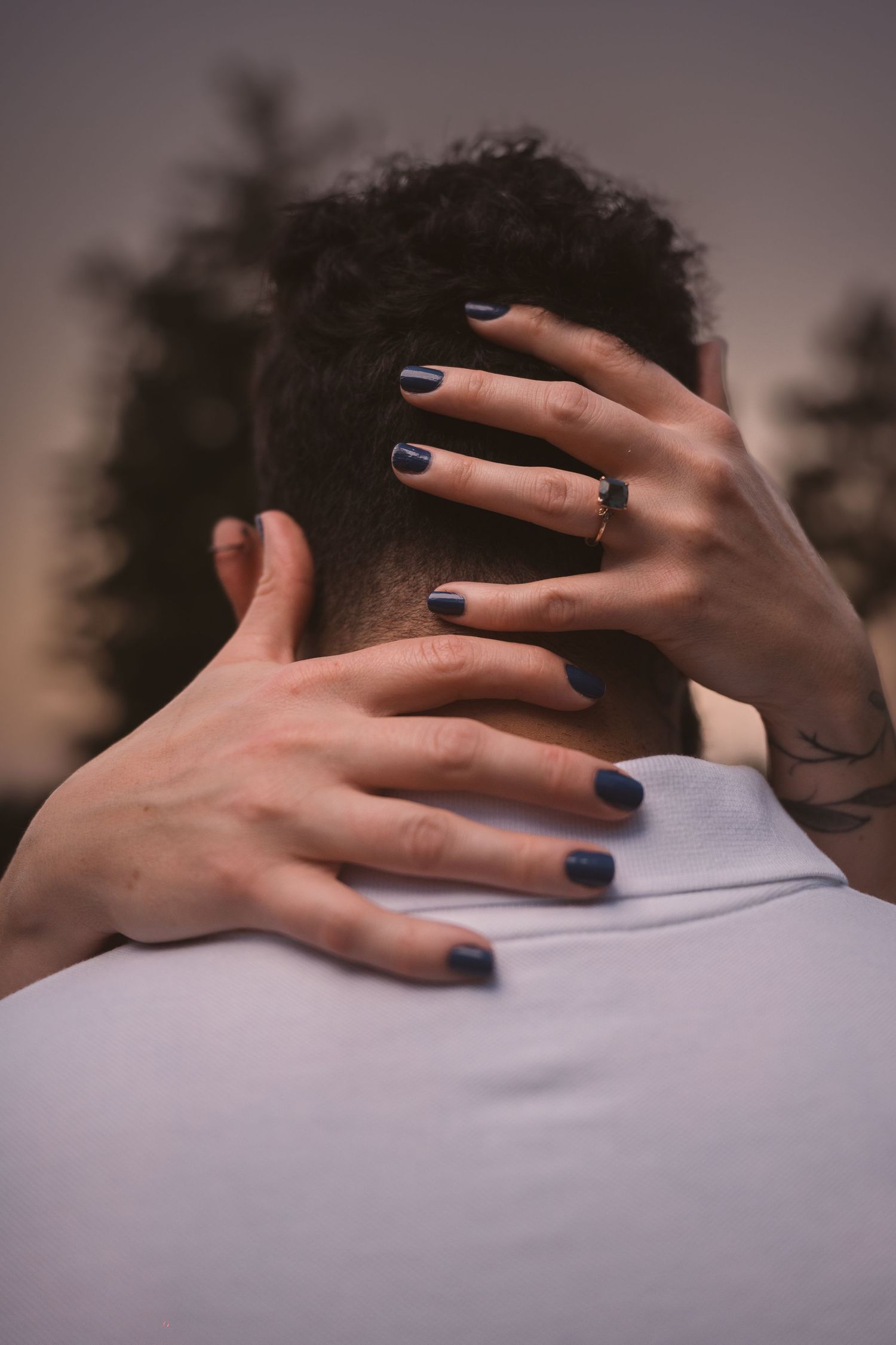 A hand with dark blue nail polish gently rests on a gray shirt, creating an intimate moment.