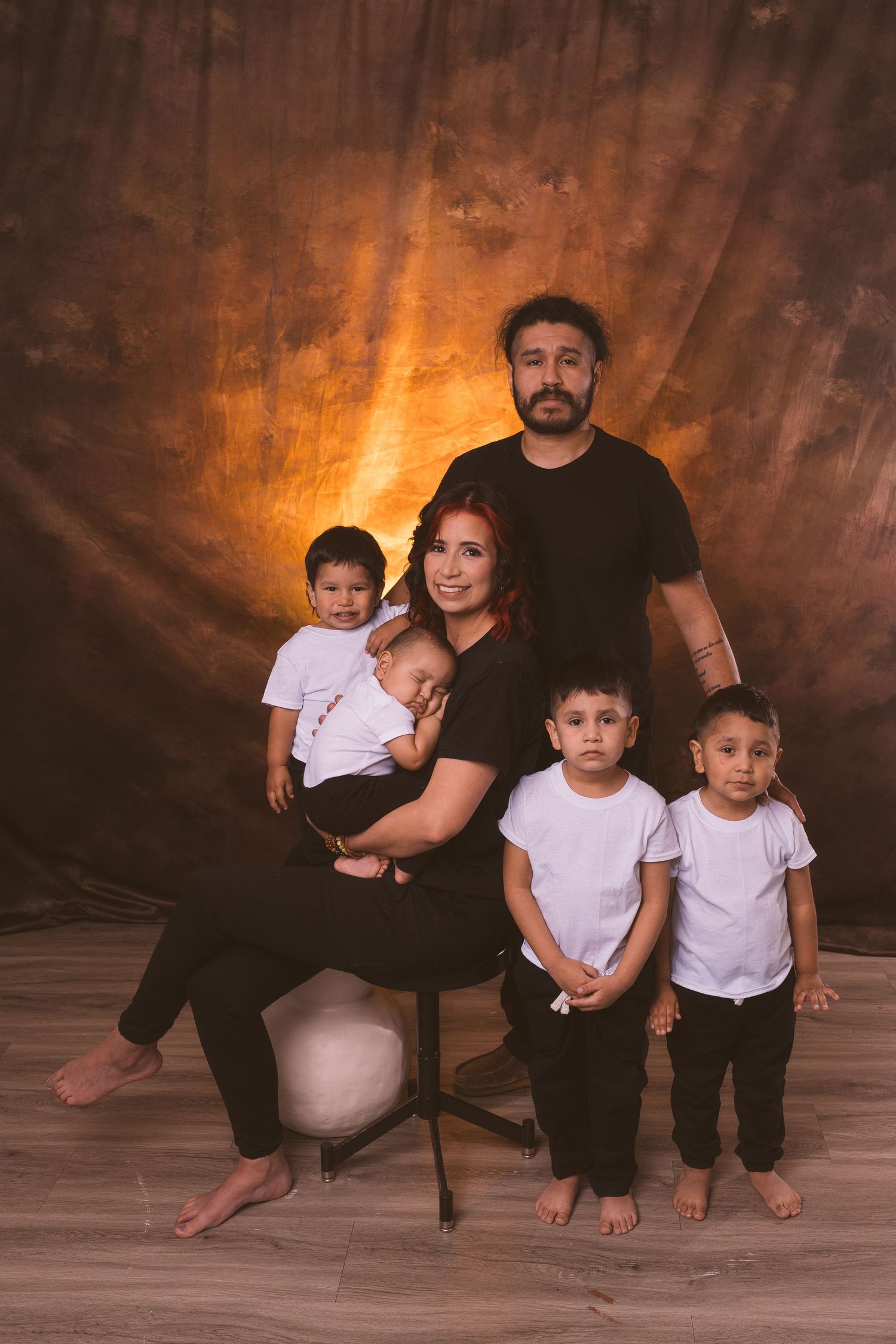 Family portrait with children in white shirts against warm brown backdrop.