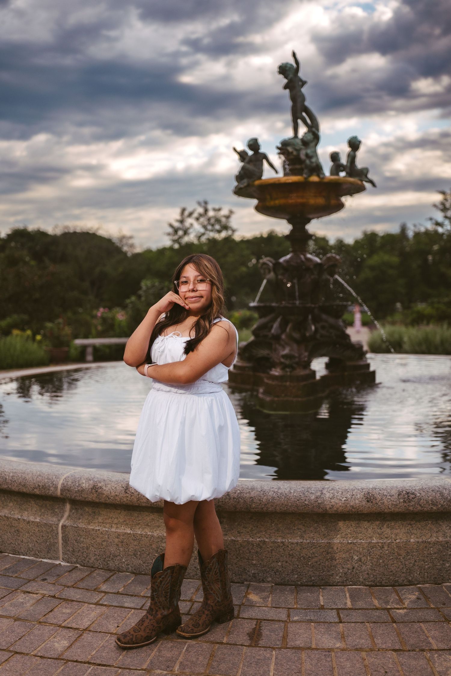 White dress and cowboy boots by an ornate fountain under dramatic evening skies.