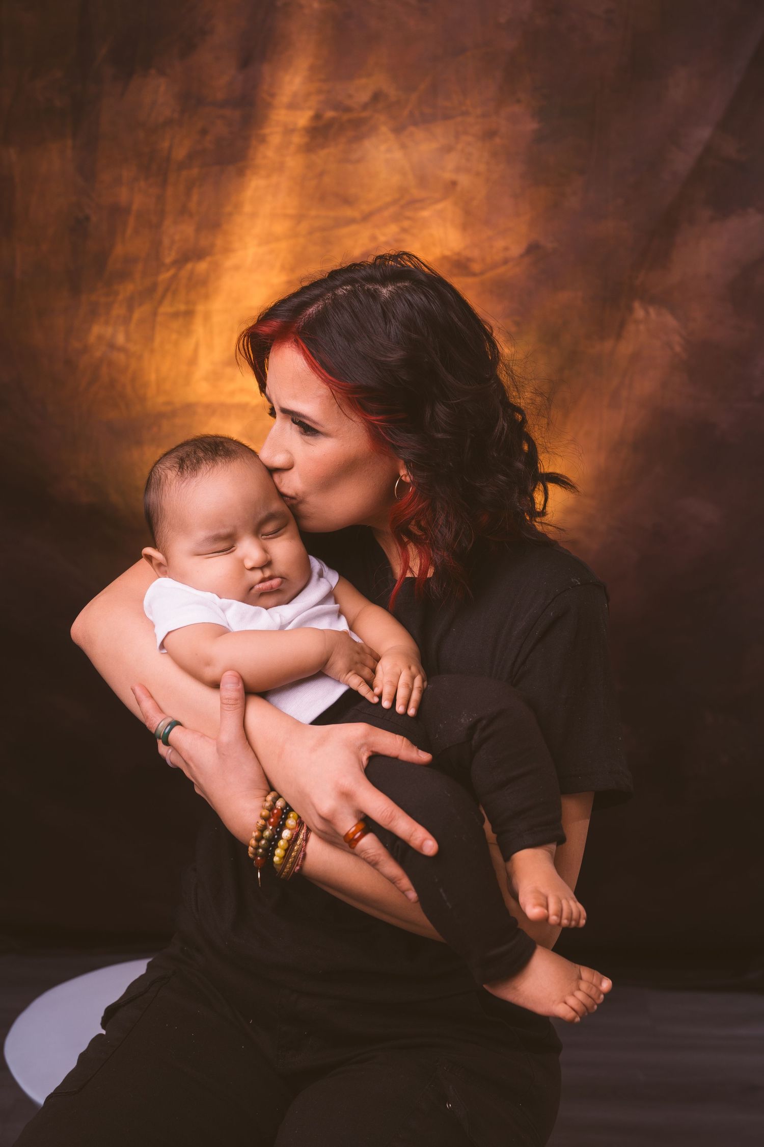Tender moment between parent and infant against dark rustic background.