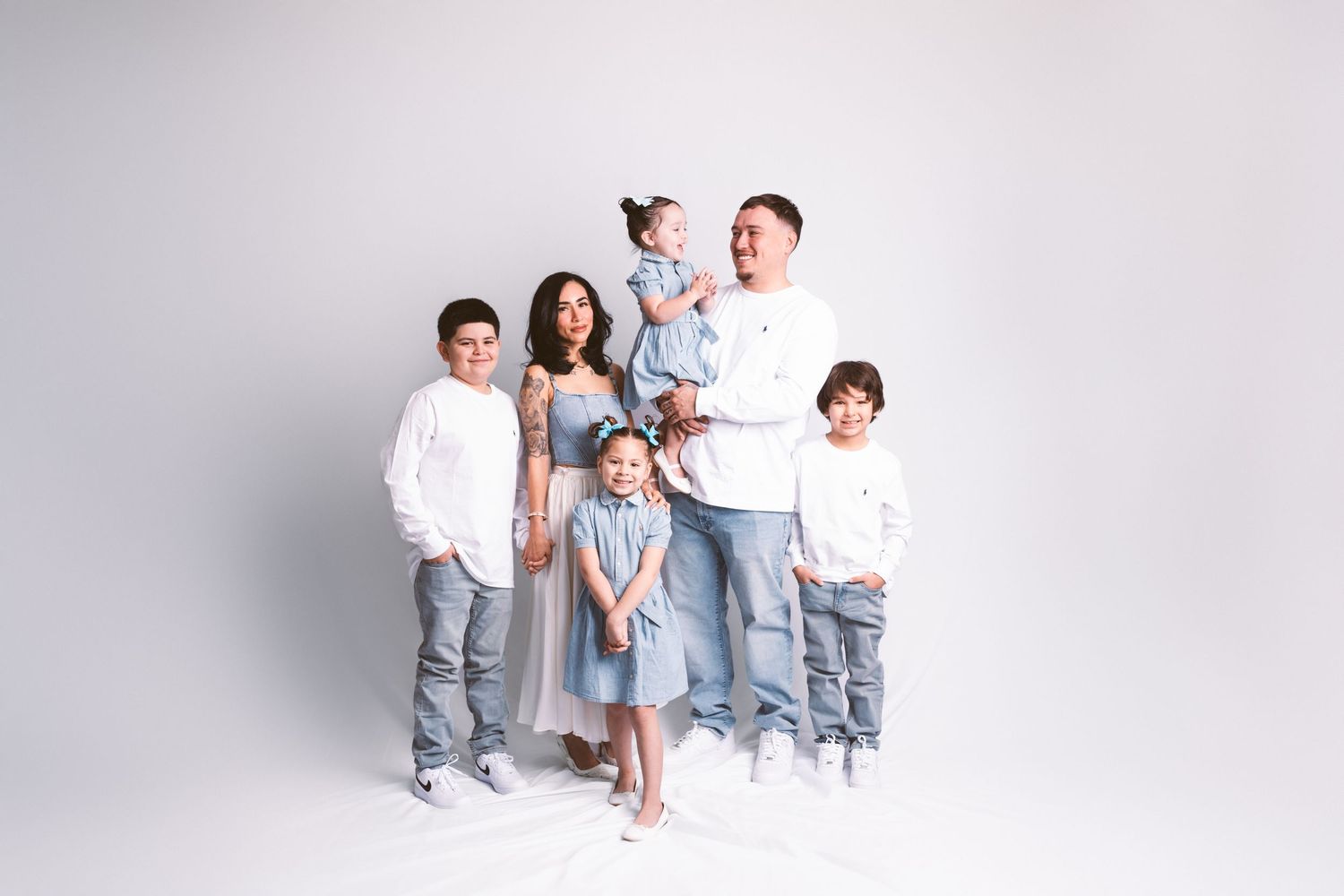 A family wearing coordinated white and light blue outfits poses together against a white background.