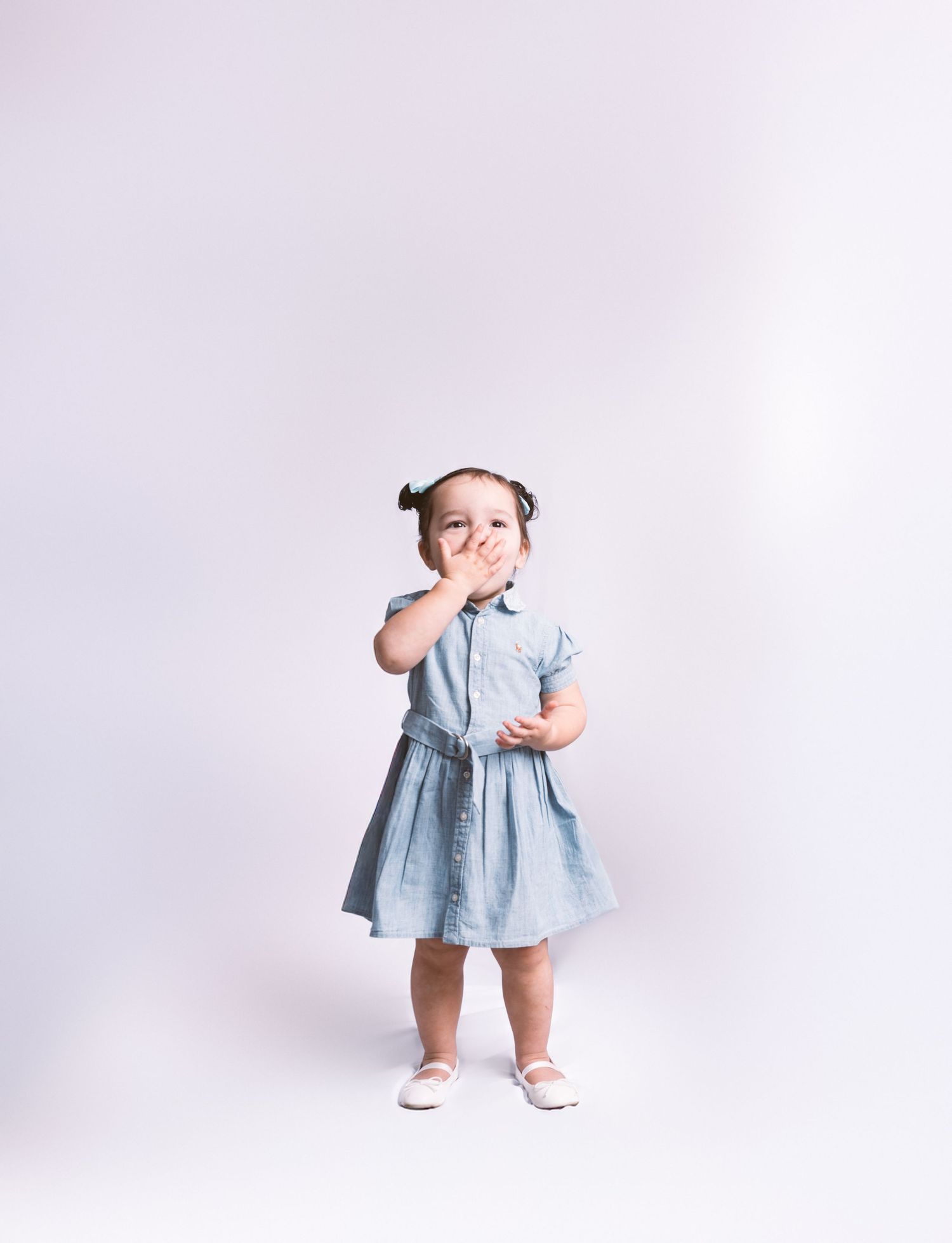 A small child in a blue dress makes playful expressions while posing in a studio setting.