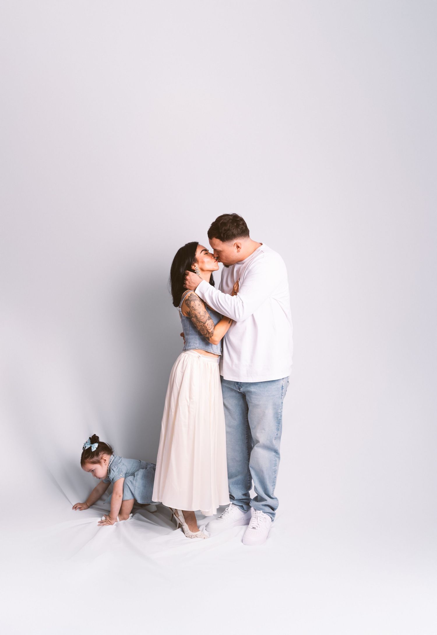 A couple in light-colored outfits shares intimate poses against a white backdrop in a romantic photo series.