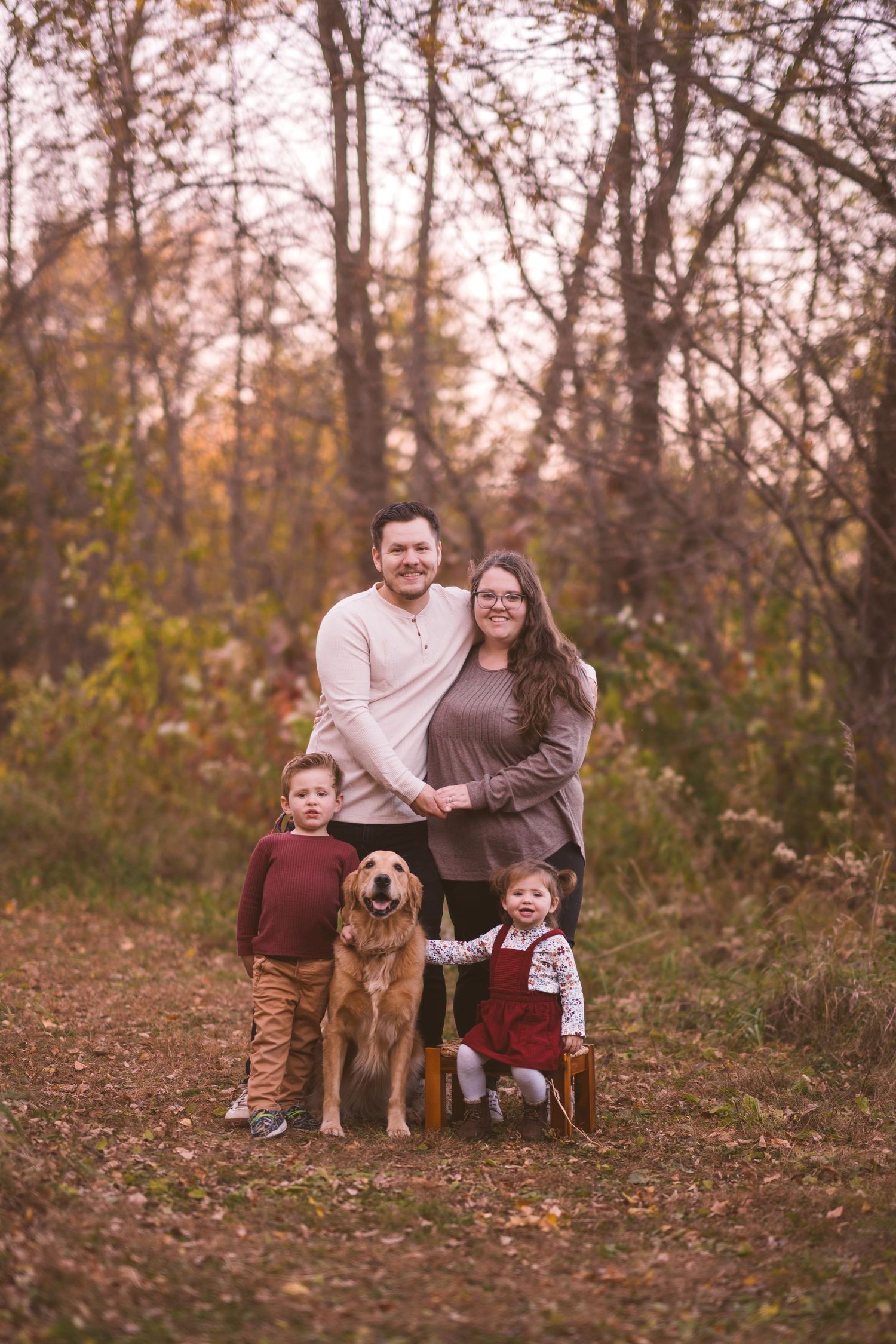 Family and pet dog pose together on hill covered in fallen autumn leaves.