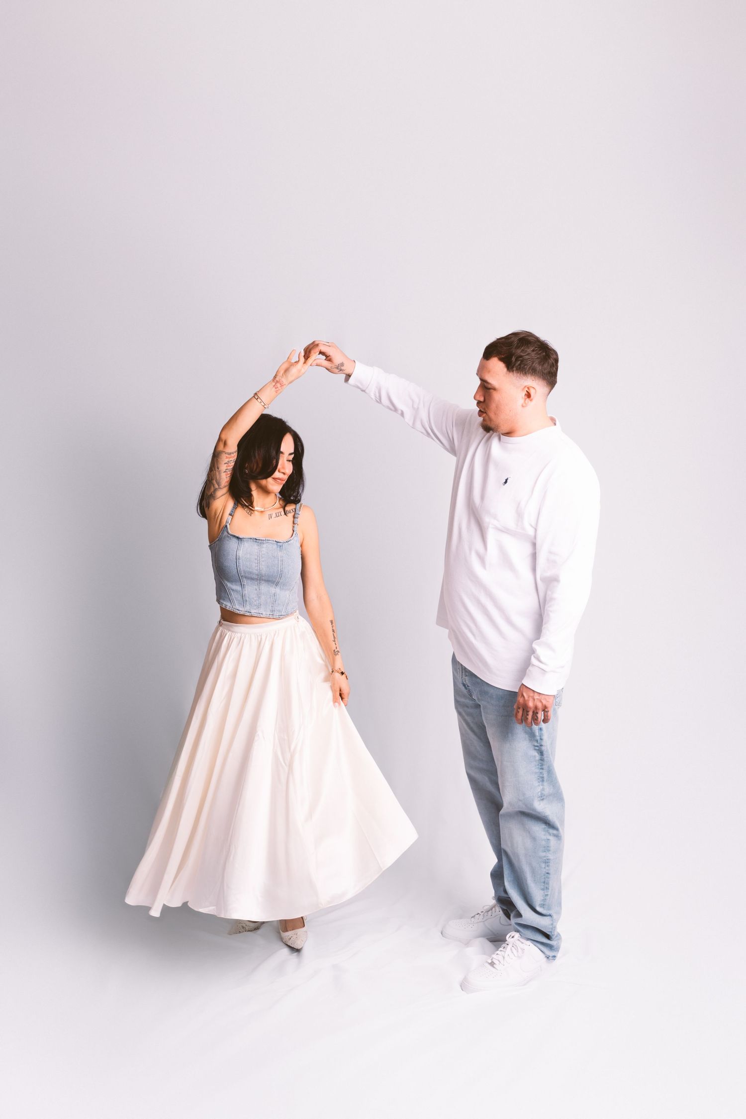 A couple dancing together against a white background, with her wearing a flowing skirt and him in casual attire.