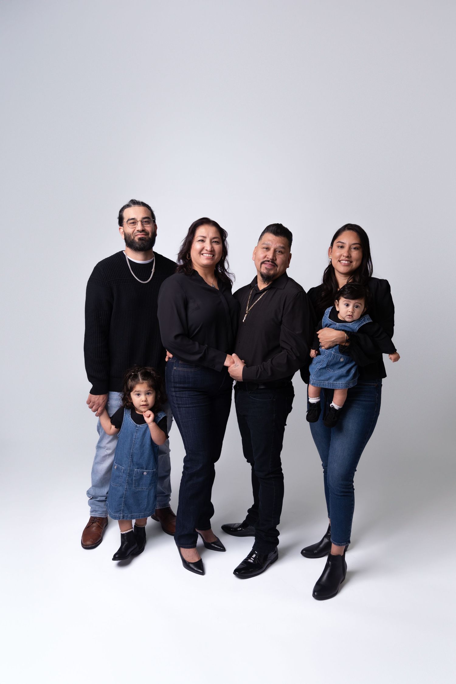 Family group photo with adults and children arranged in casual poses against white background.