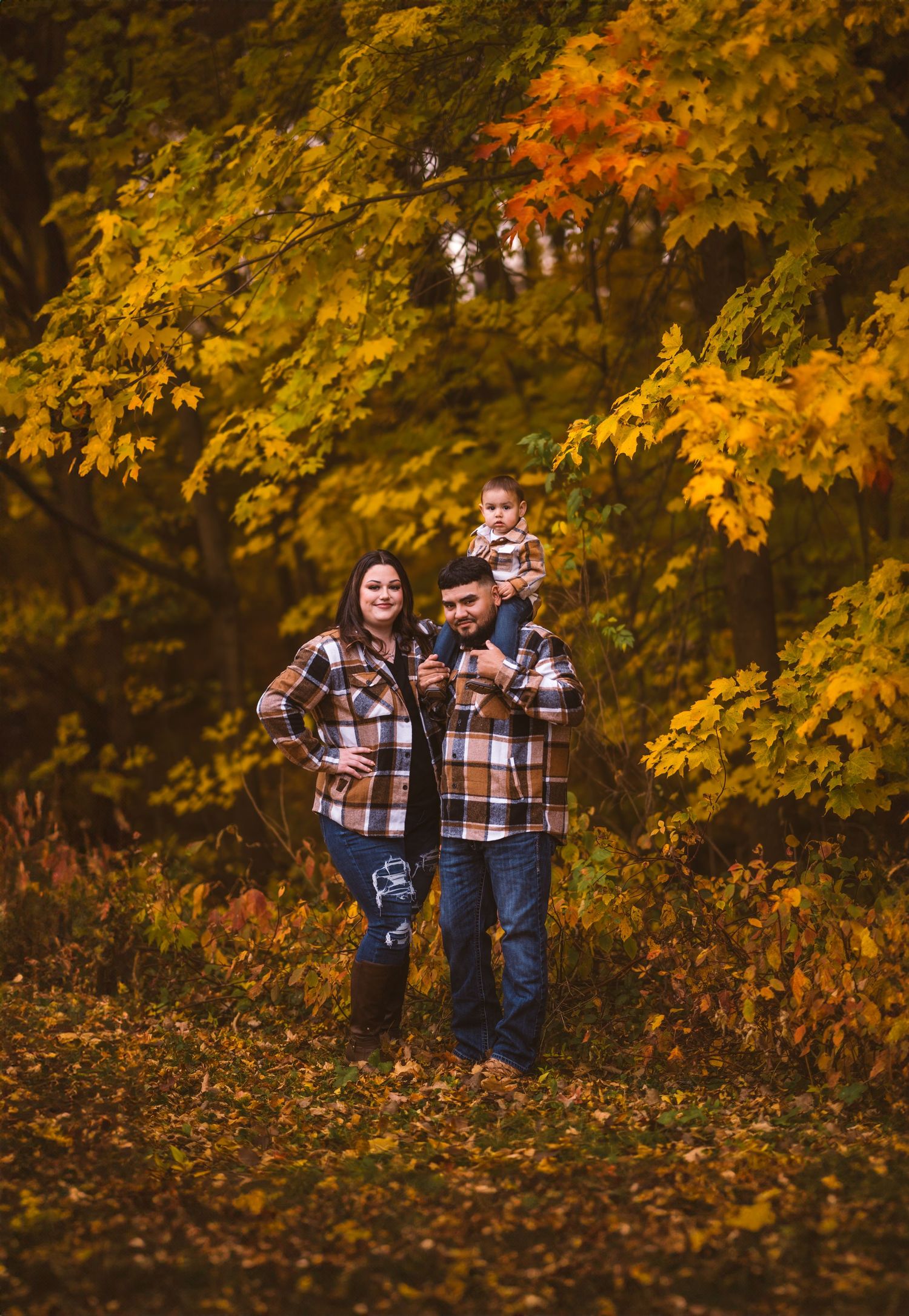A family group poses together on fallen leaves with vibrant autumn trees in the background.