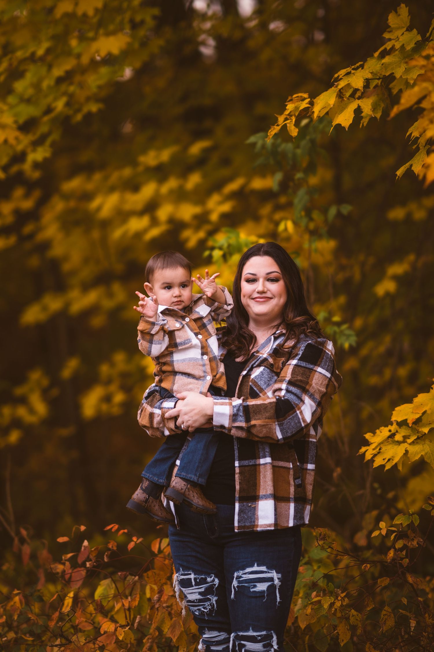 Family wearing matching plaid shirts embrace against a backdrop of fall foliage.