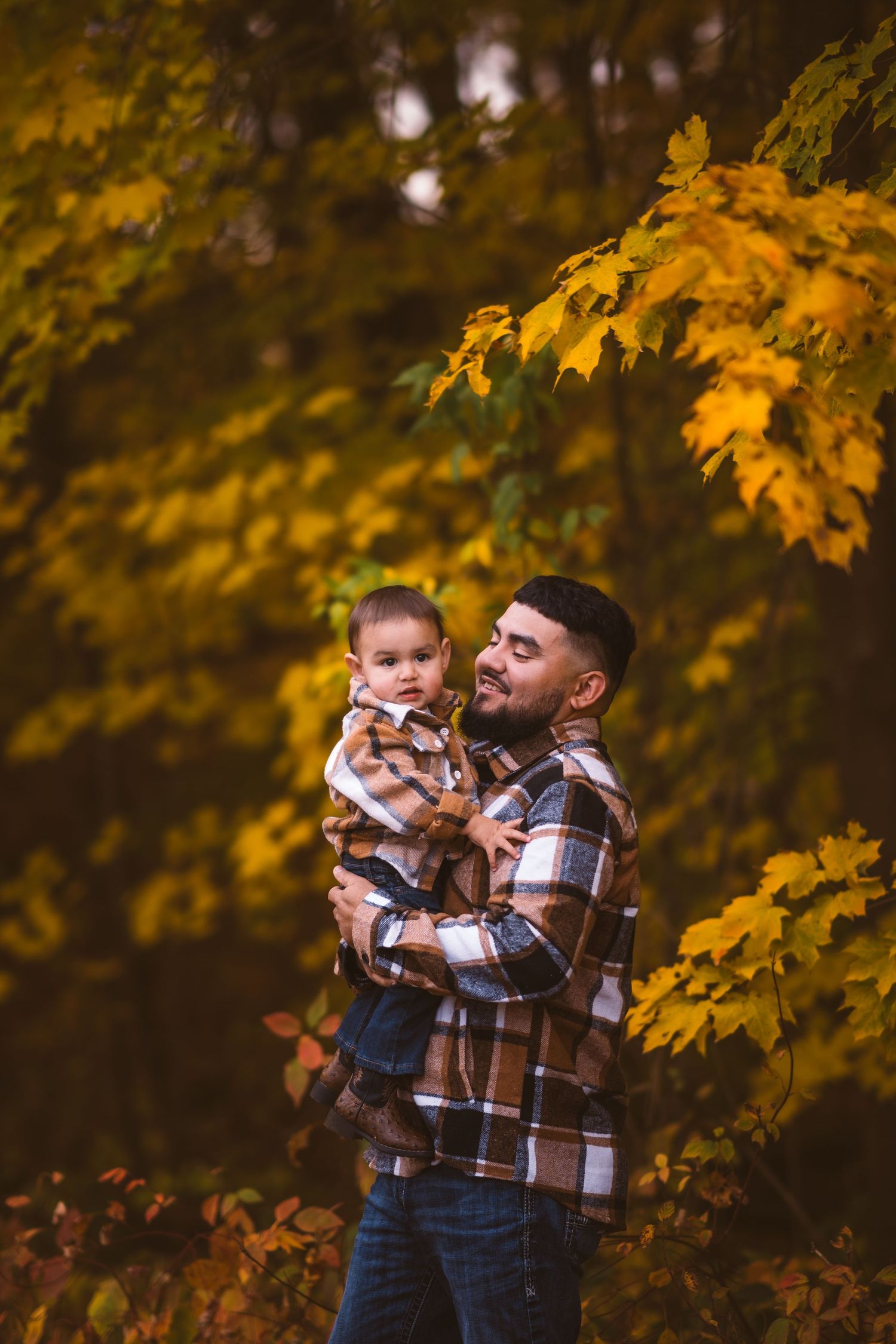 Sweet family moment captured in front of vibrant yellow fall leaves.