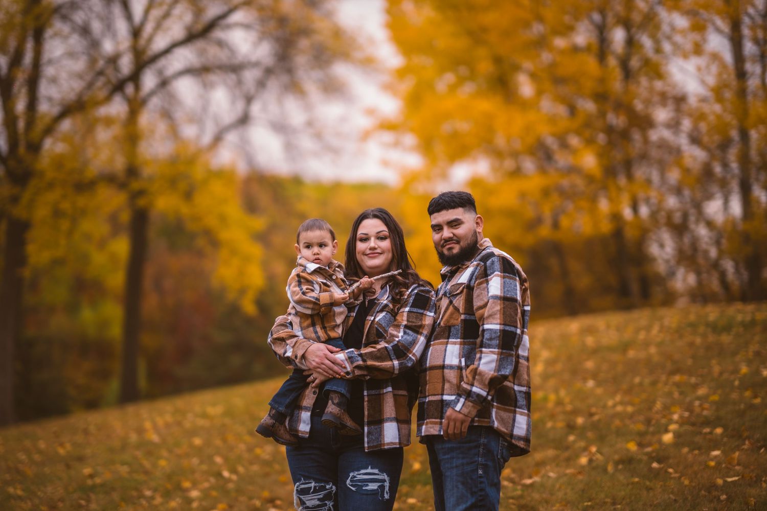 Three people in coordinated plaid outfits walk together through a golden autumn landscape.