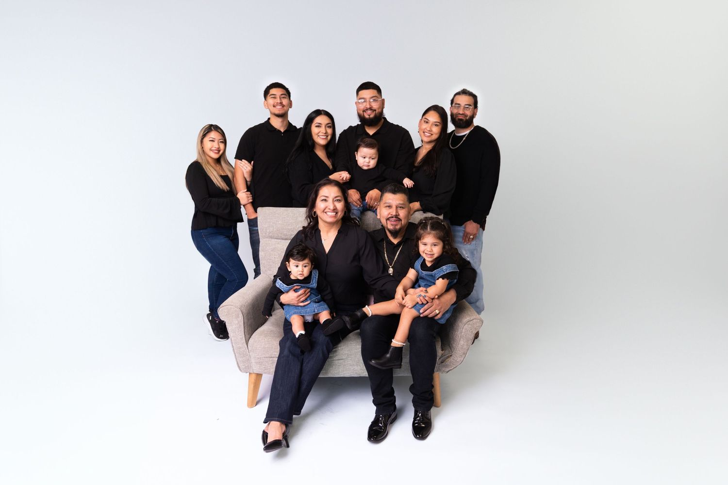 Family poses together on white backdrop wearing coordinated outfits for holiday photos.