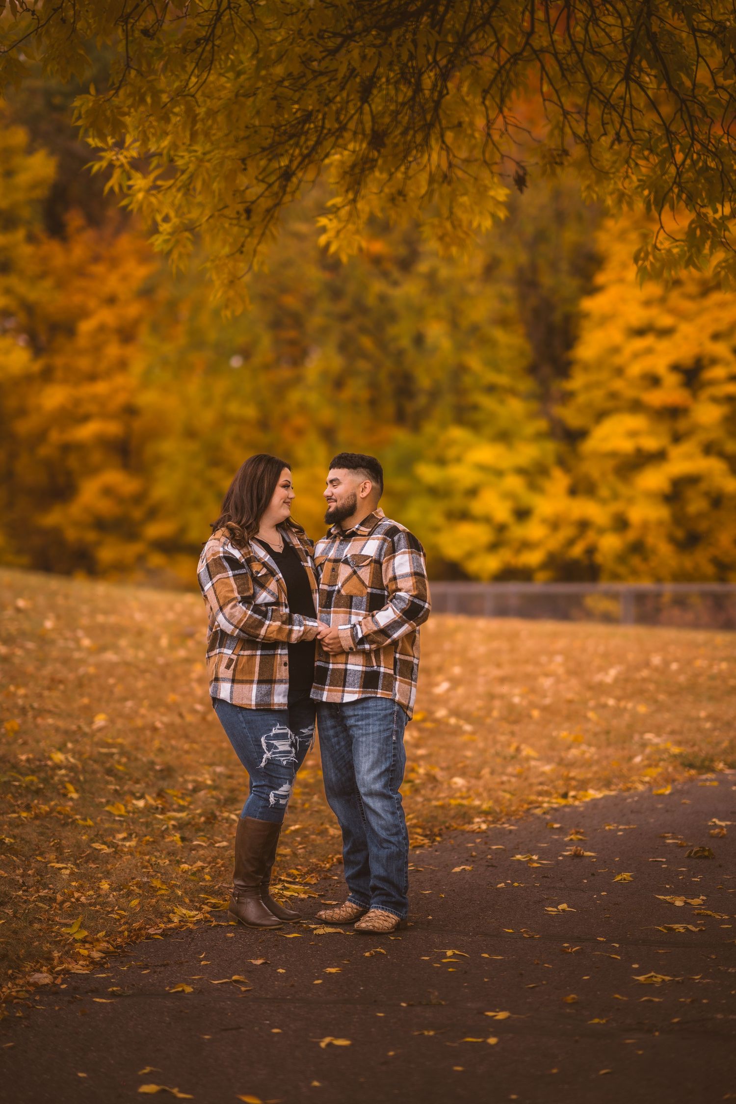 Couple in coordinated plaid outfits share a romantic moment among autumn leaves.