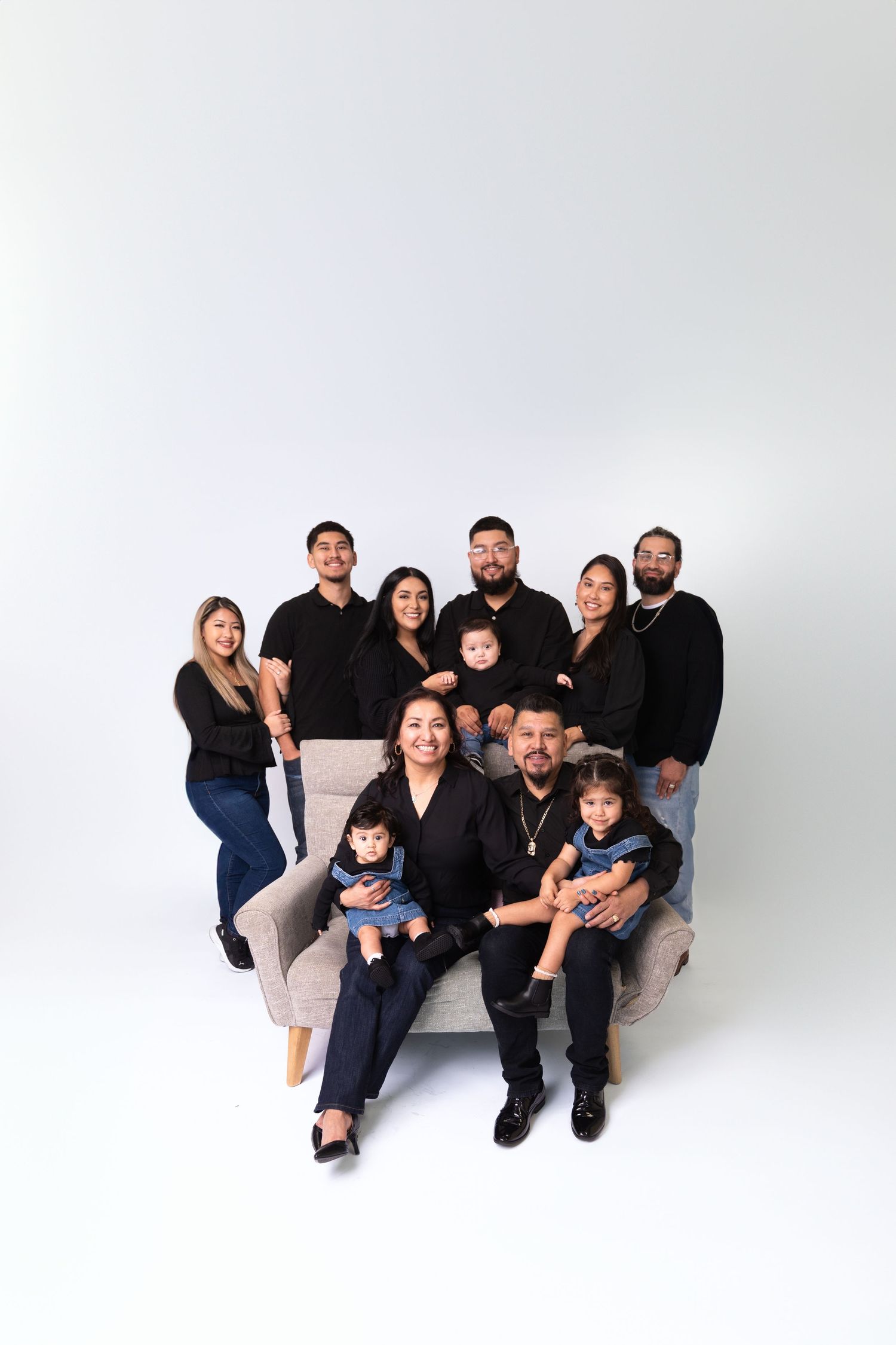Extended family portrait with multiple generations posed together on white backdrop.