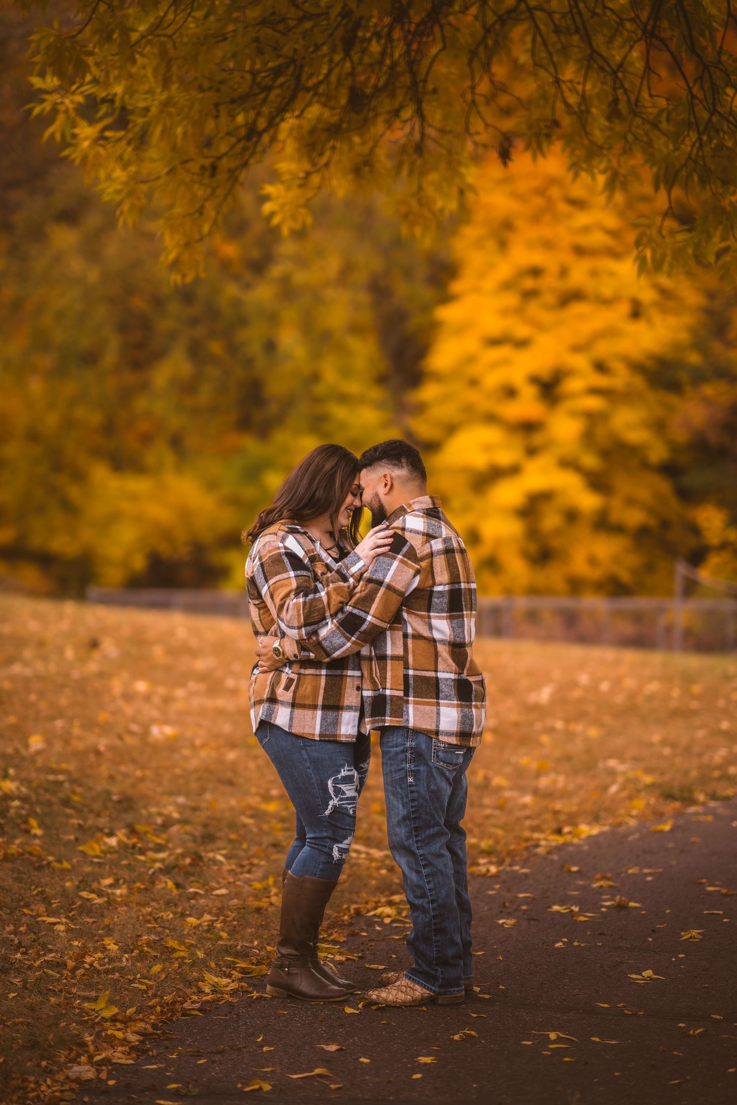 Couple embracing on path covered with fallen autumn leaves.