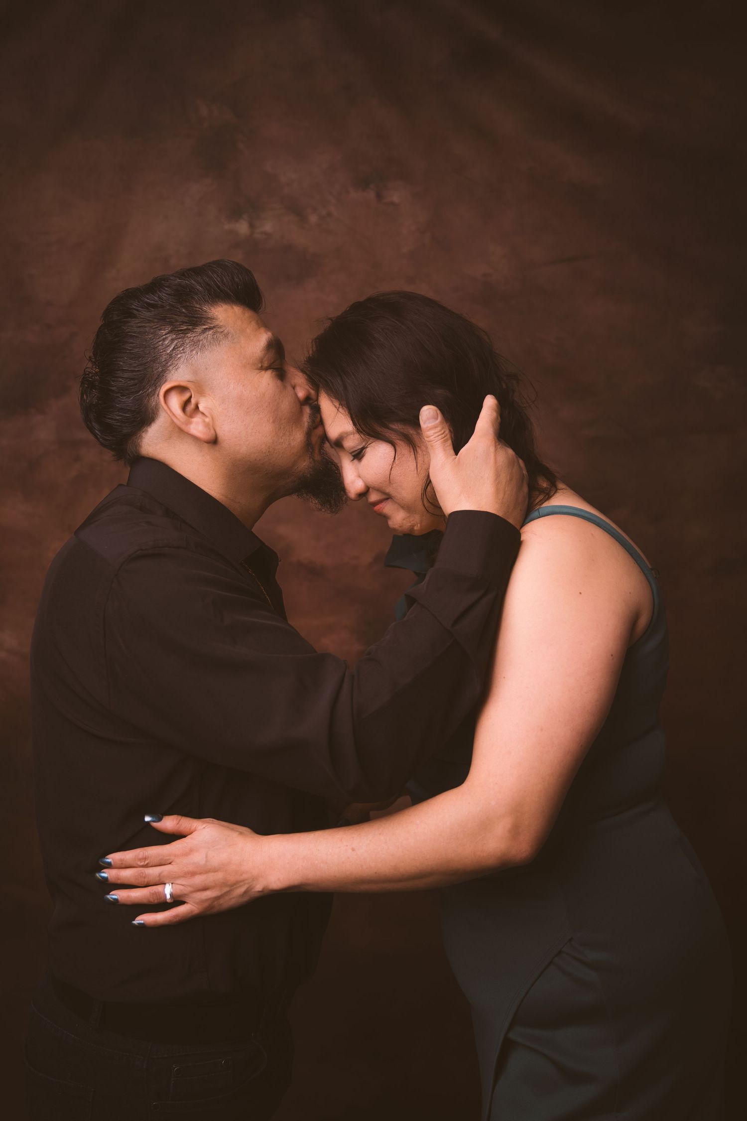 Intimate couple portrait in dark studio setting with dramatic lighting.