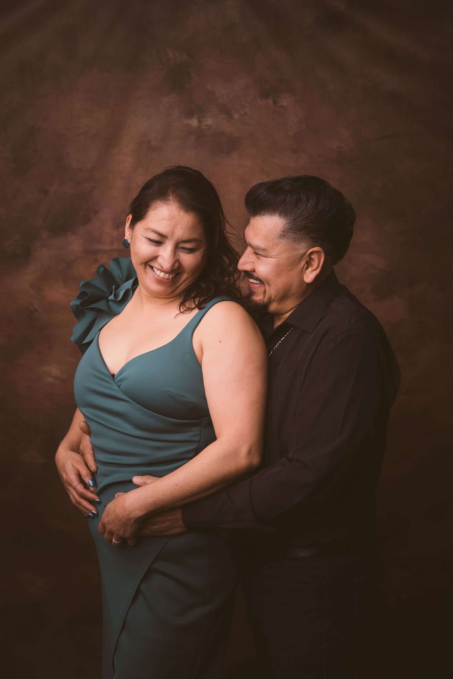 Couple shares tender moment in studio with dramatic lighting and dark background.