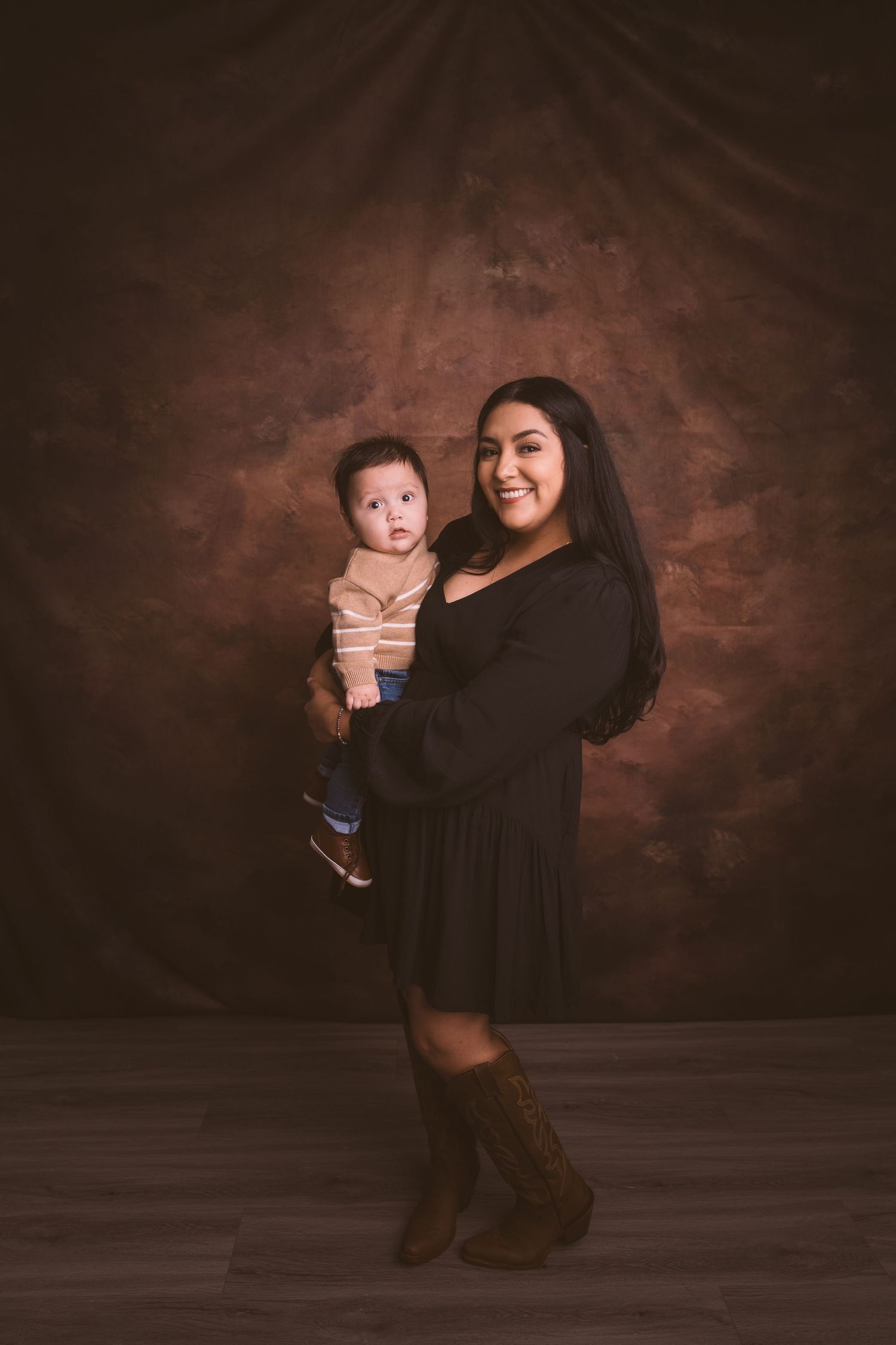 A dark moody photo series showing a baby being lifted and held against a brown backdrop.