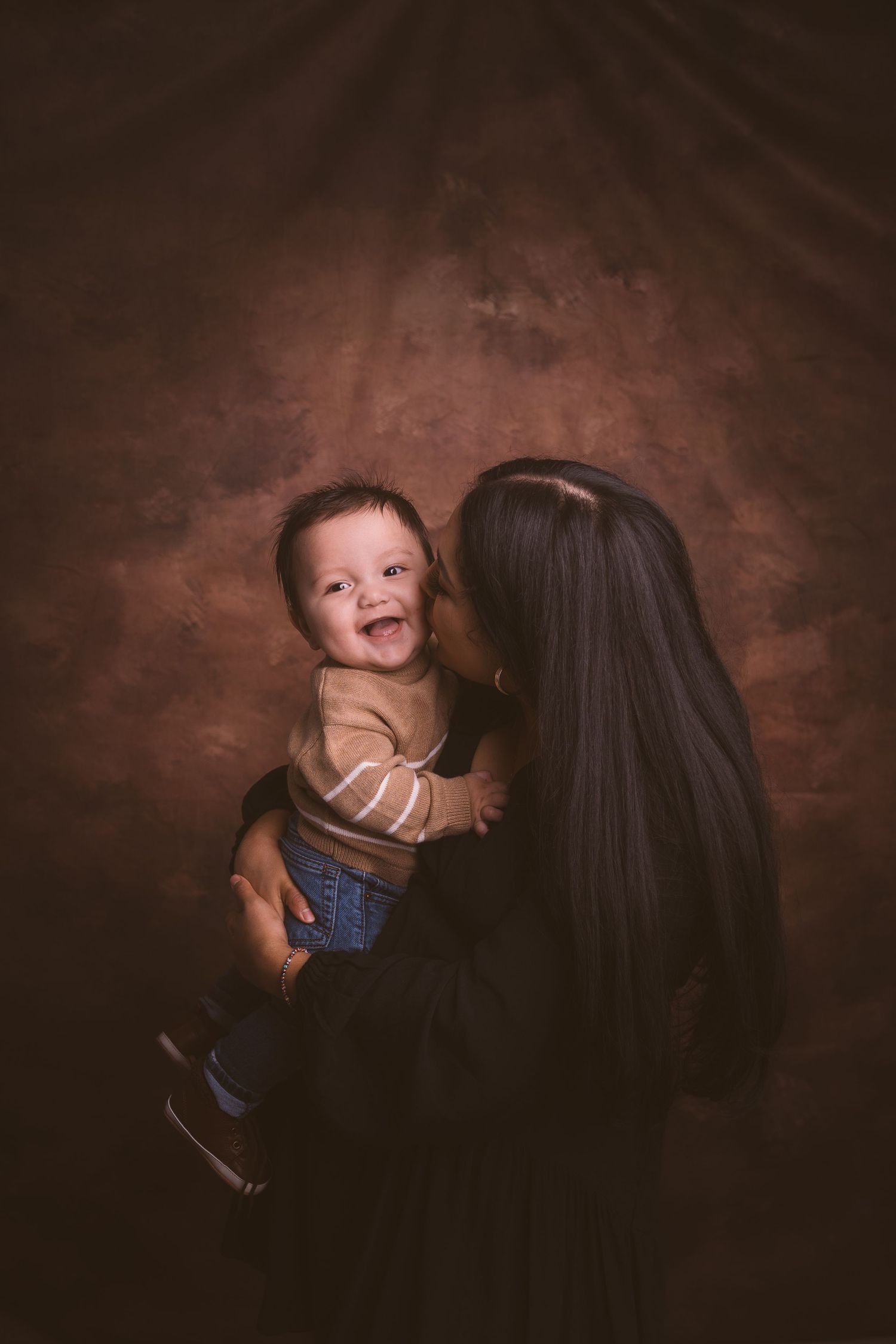 Playful sequence of a baby being lifted up in front of a dark brown studio backdrop.