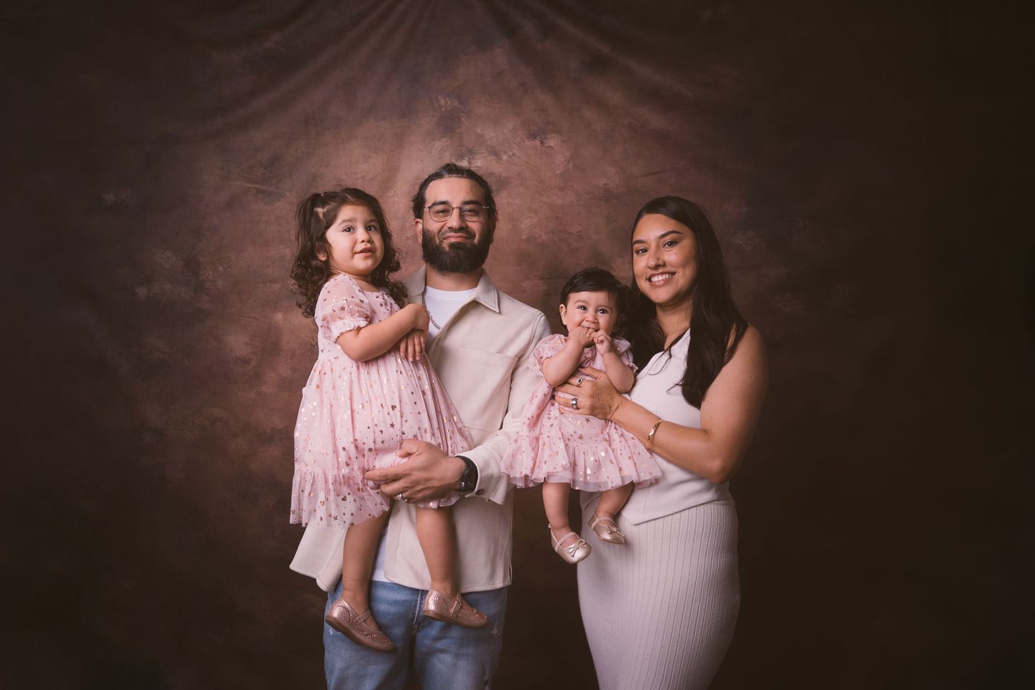 A family of three poses in coordinated outfits against a dark brown backdrop.