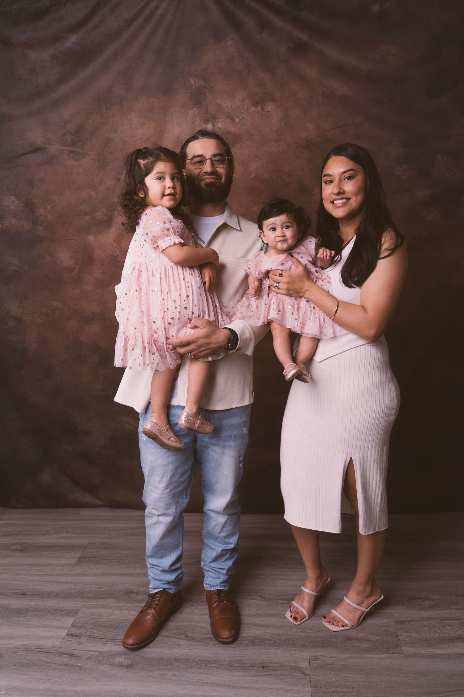 A family wearing coordinated pink and white outfits poses together in a studio setting.