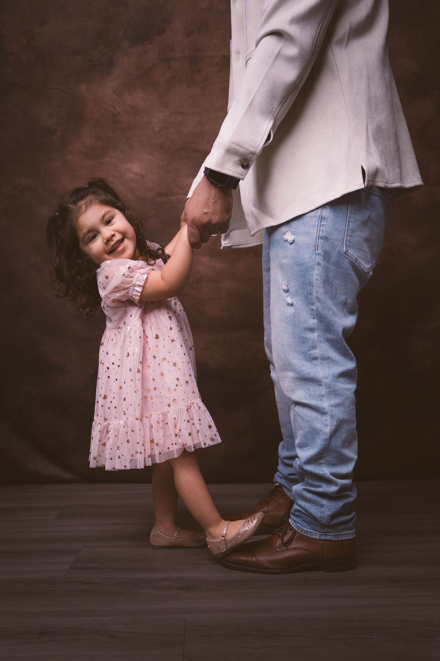 A playful dance-like pose between adult and child wearing coordinated light-colored outfits.