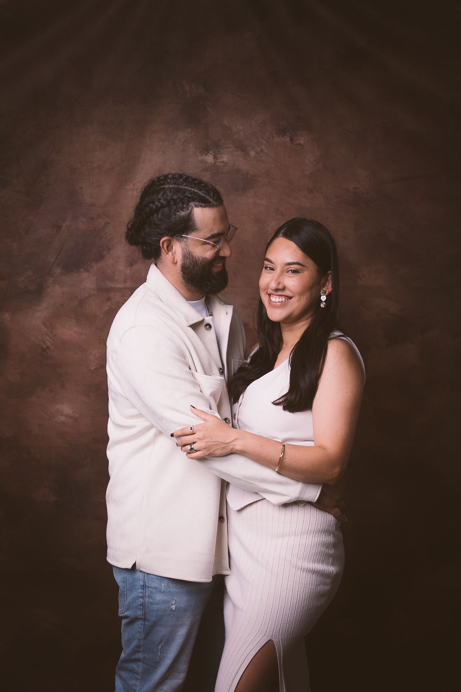 A joyful couple embracing in a studio setting against a textured brown backdrop.