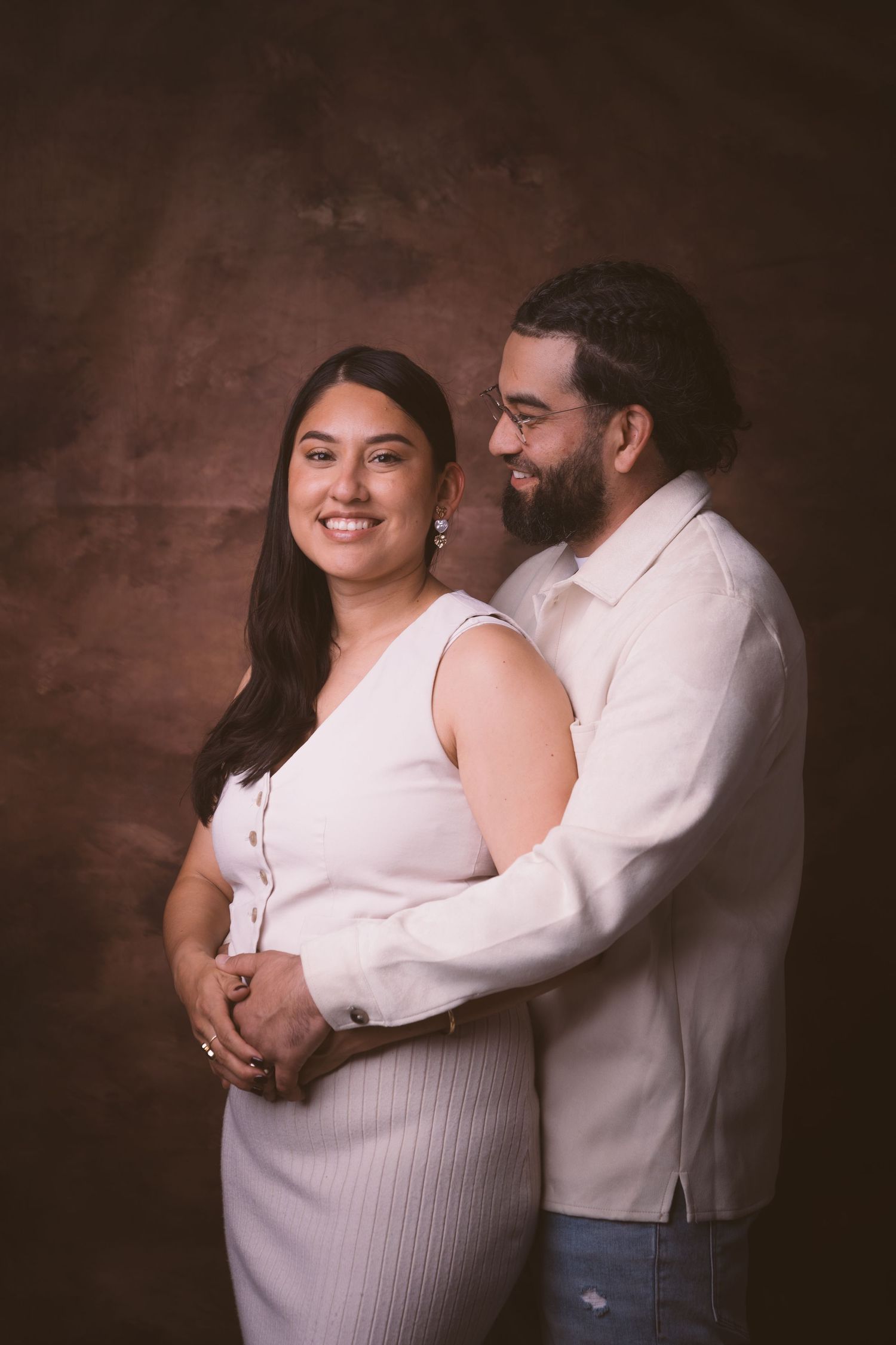 A warm embrace captured in studio lighting with both wearing complementary light-colored outfits.
